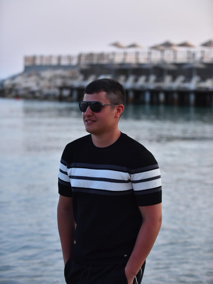 Ahmet Babuşçu, co-founder of GrowFire Studios, standing by the water wearing sunglasses and a black t-shirt, representing the GrowFire team.