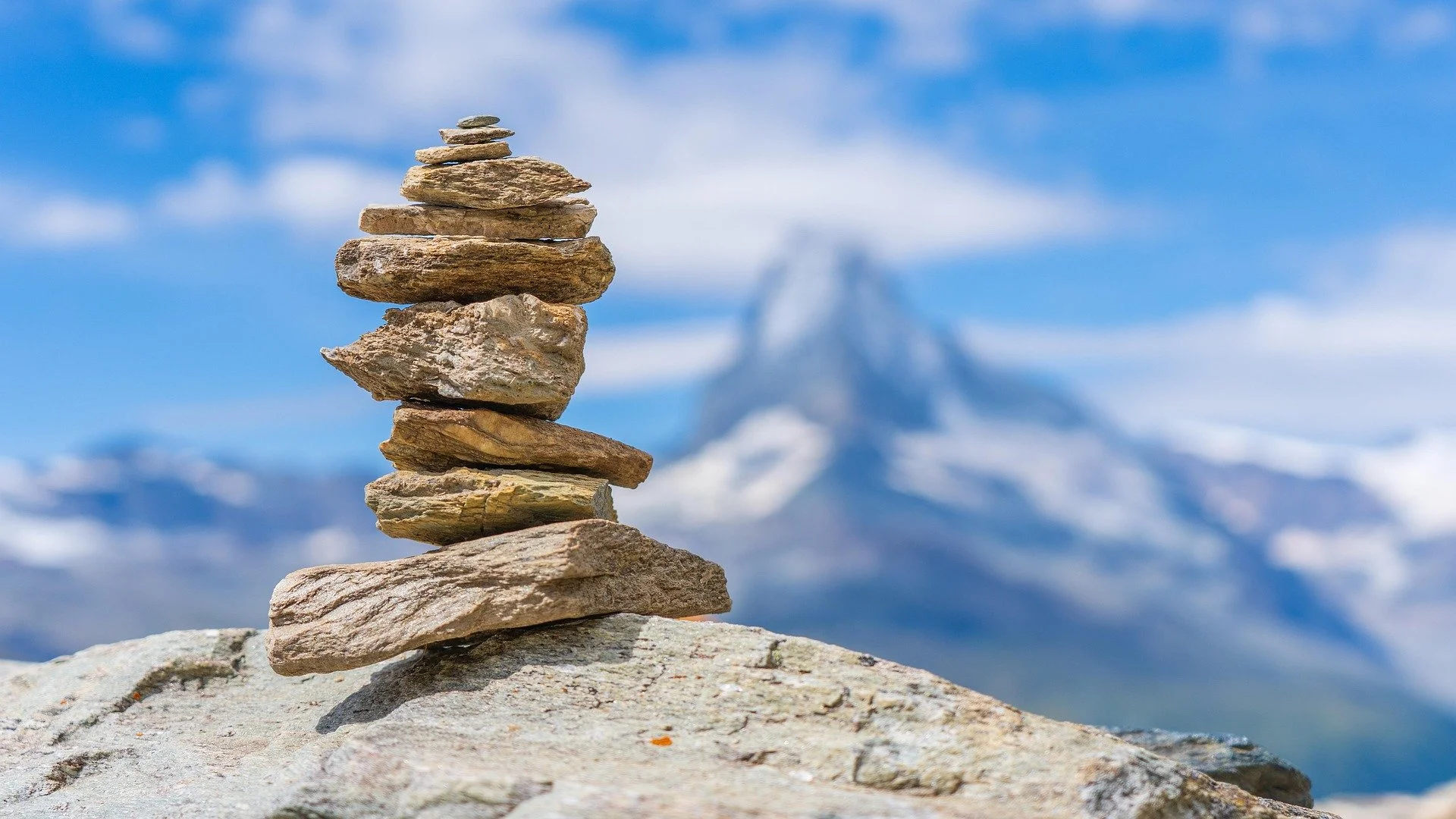 Stacked rocks in foreground with snow-capped mountain and blue sky in background.