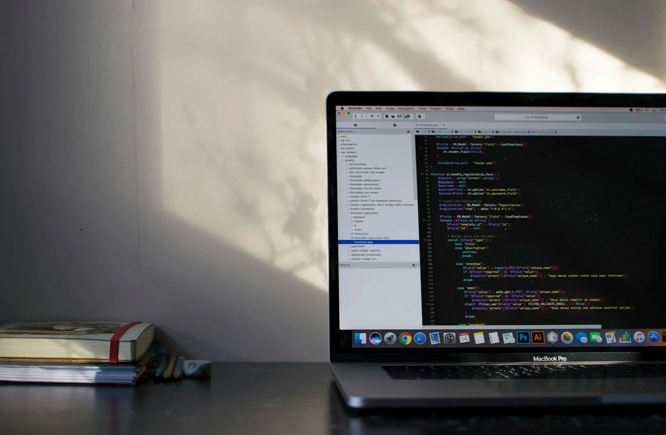 Close-up of a computer screen displaying code, with a desk at the bottom showing stacked notebooks and a MacBook Pro.