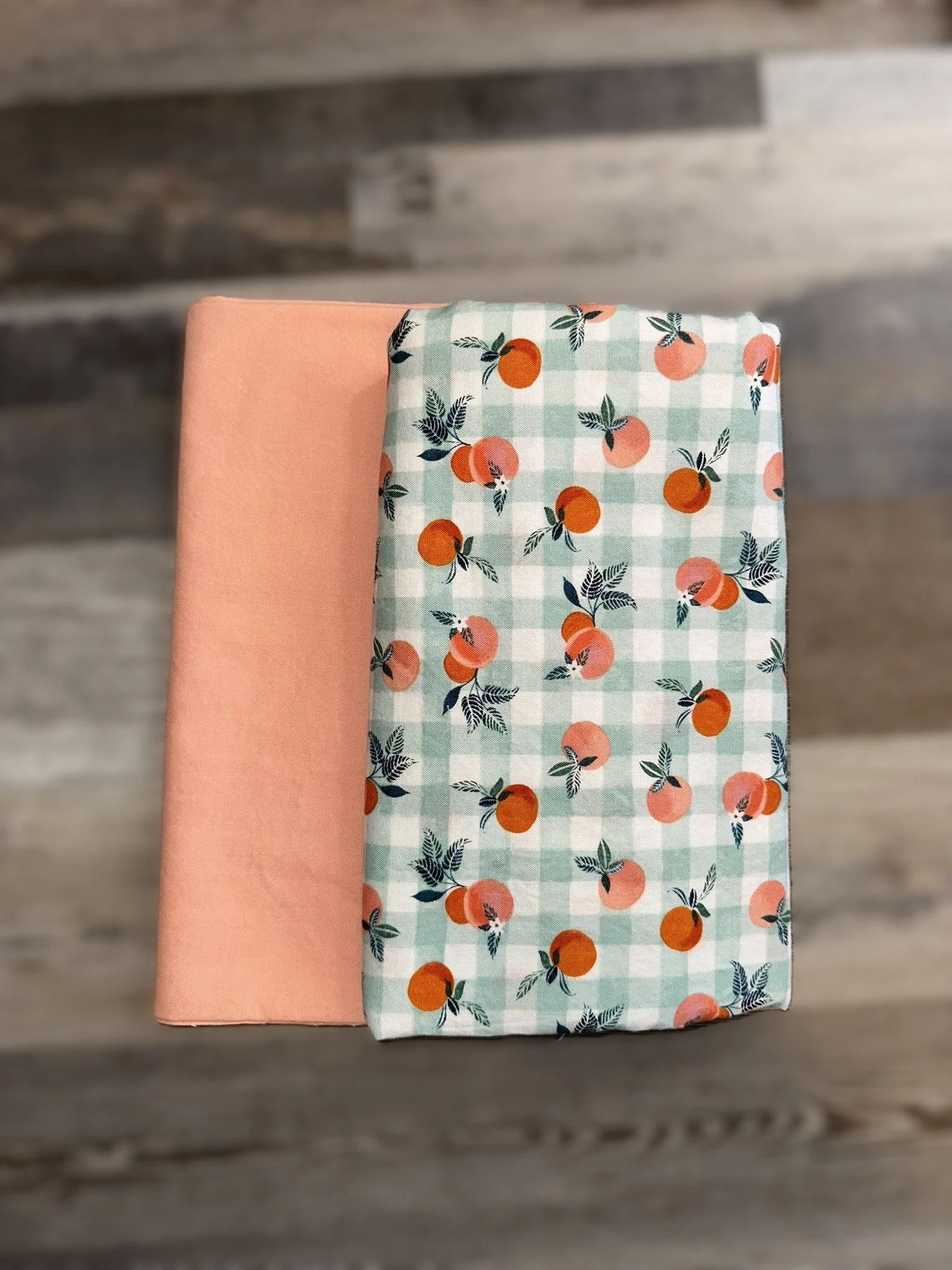 Two folded fabrics, one in plain peach color and the other with a peach and leaf pattern on a green and white checkered background.