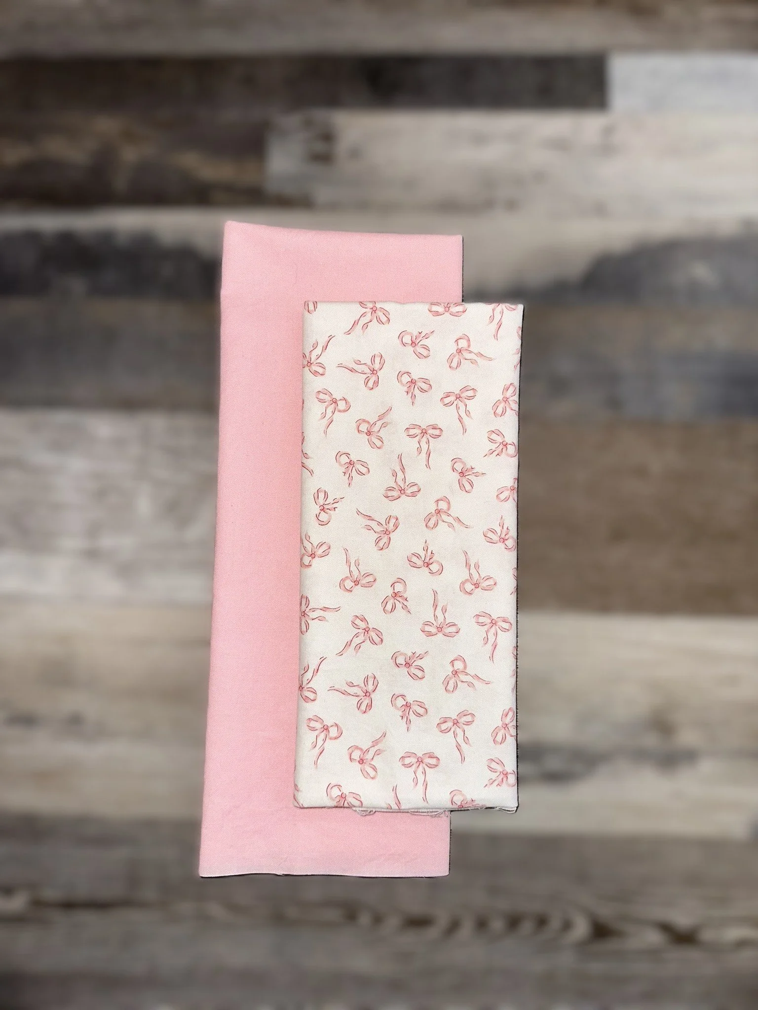 Two folded cloths, one pink and one white with pink ribbons pattern, placed on a wooden surface.