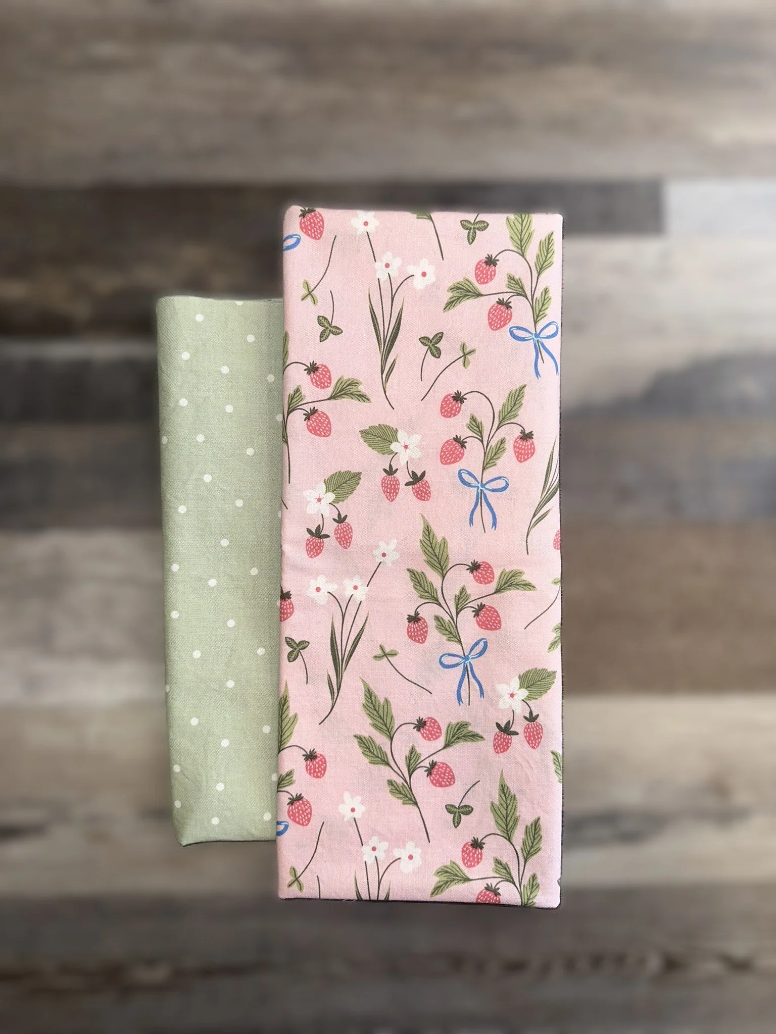 Two wrapped gift boxes, one with a pink strawberry pattern and the other with a light green polka dot pattern, on a wooden surface.