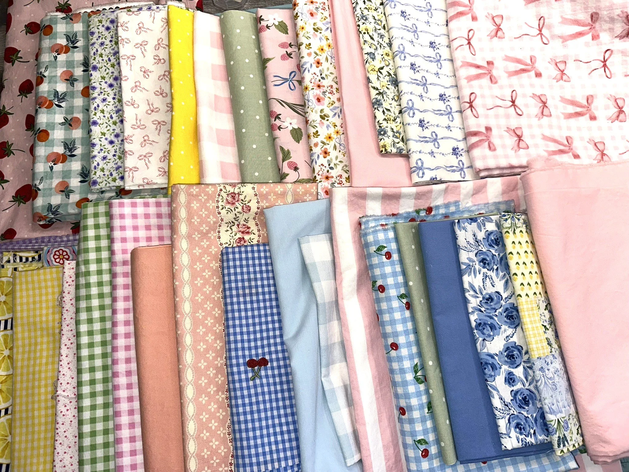 Assorted fabric pieces with various floral, checkered, and dotted patterns in pastel colors, neatly stacked on a surface.