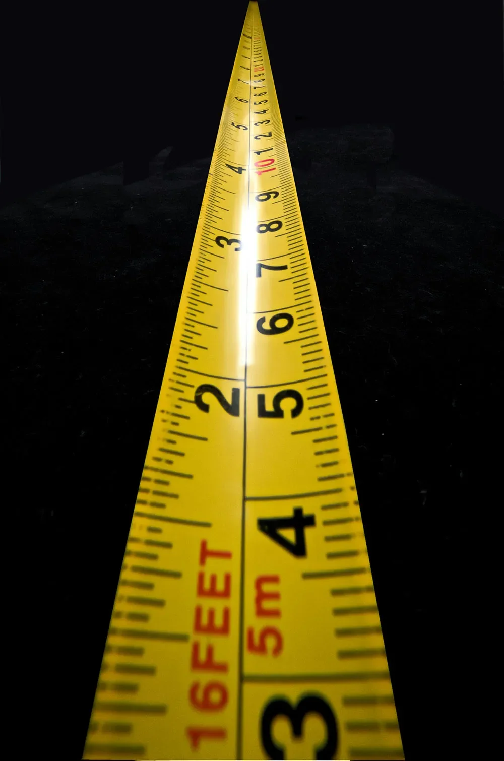 Close-up of a yellow measuring tape stretched out on a dark surface, displaying measurements from 1 to 6 inches.