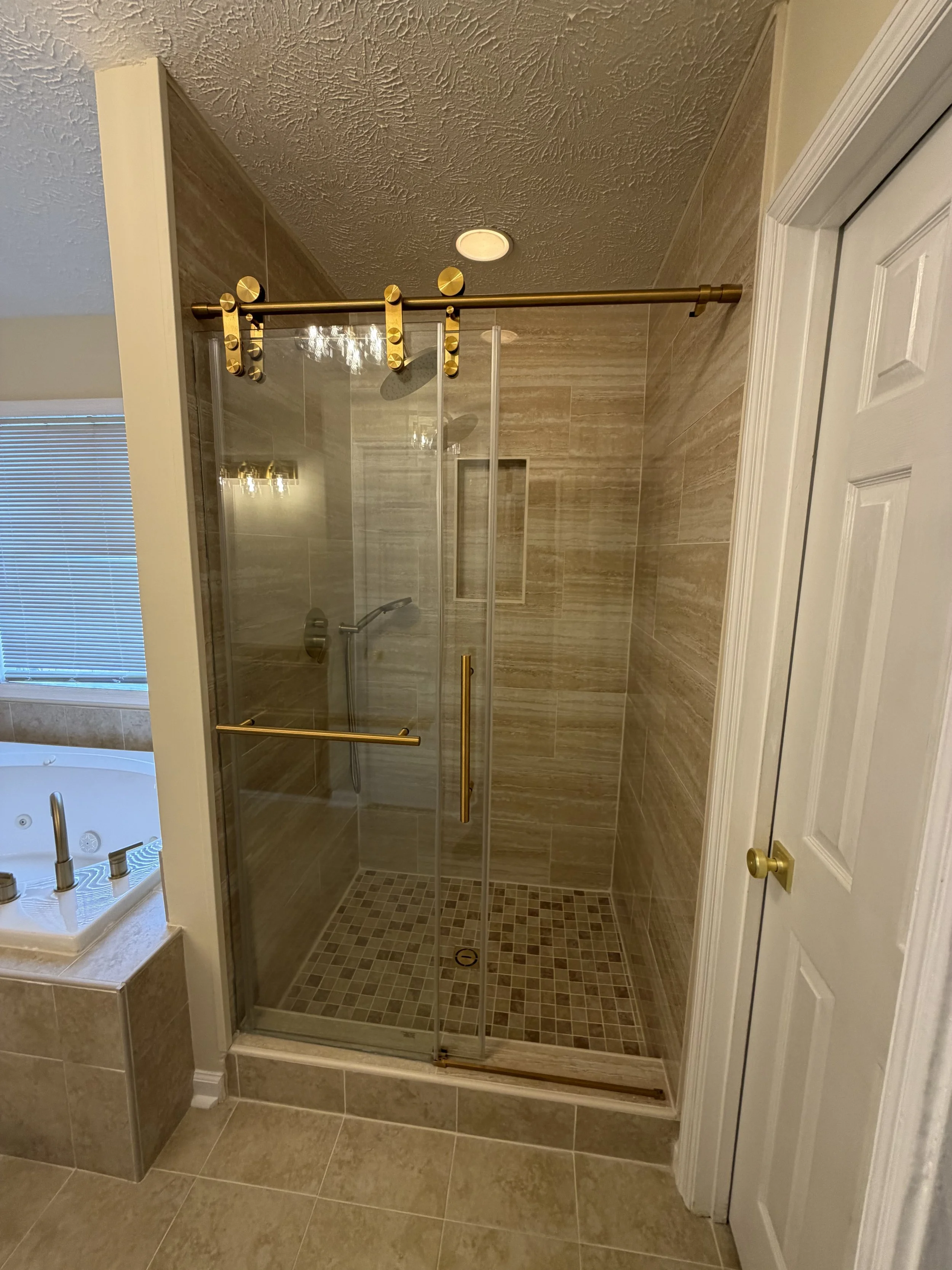 Bathroom shower with sliding glass door, gold hardware, brown tile walls, and a built-in niche in the wall.
