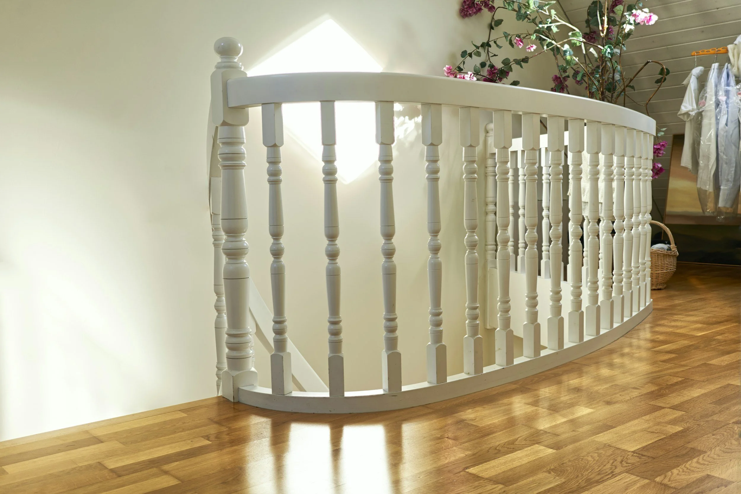 White curved staircase balustrade with wooden floor and pink flowers in the background.