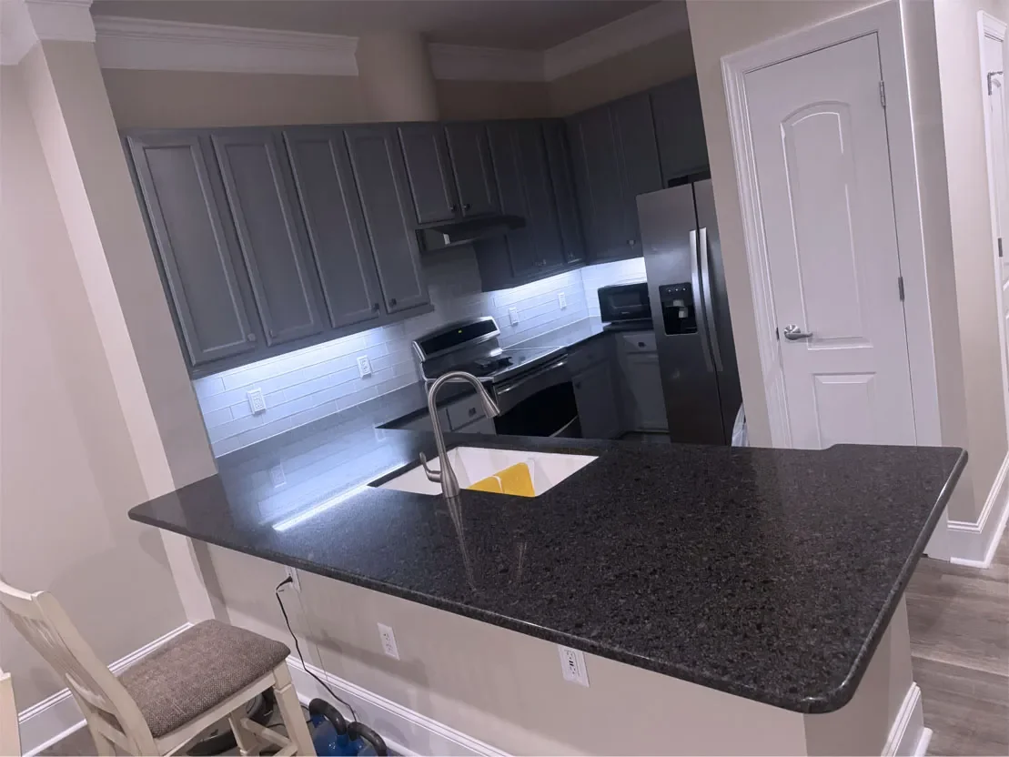 Modern kitchen with dark granite countertops, gray cabinets, stainless steel appliances, and a white subway tile backsplash.