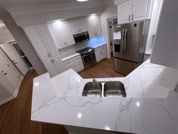 Modern kitchen with white cabinets, stainless steel refrigerator, oven, microwave, and a marble countertop island with a double-sink.