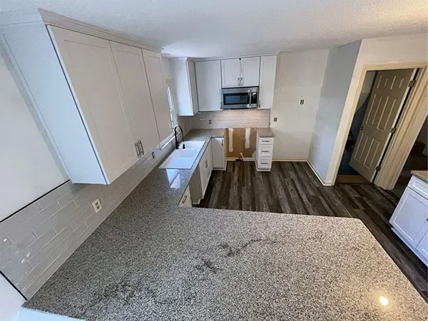 Empty kitchen with white cabinets, microwave, countertop, white sink, and dark wood flooring.