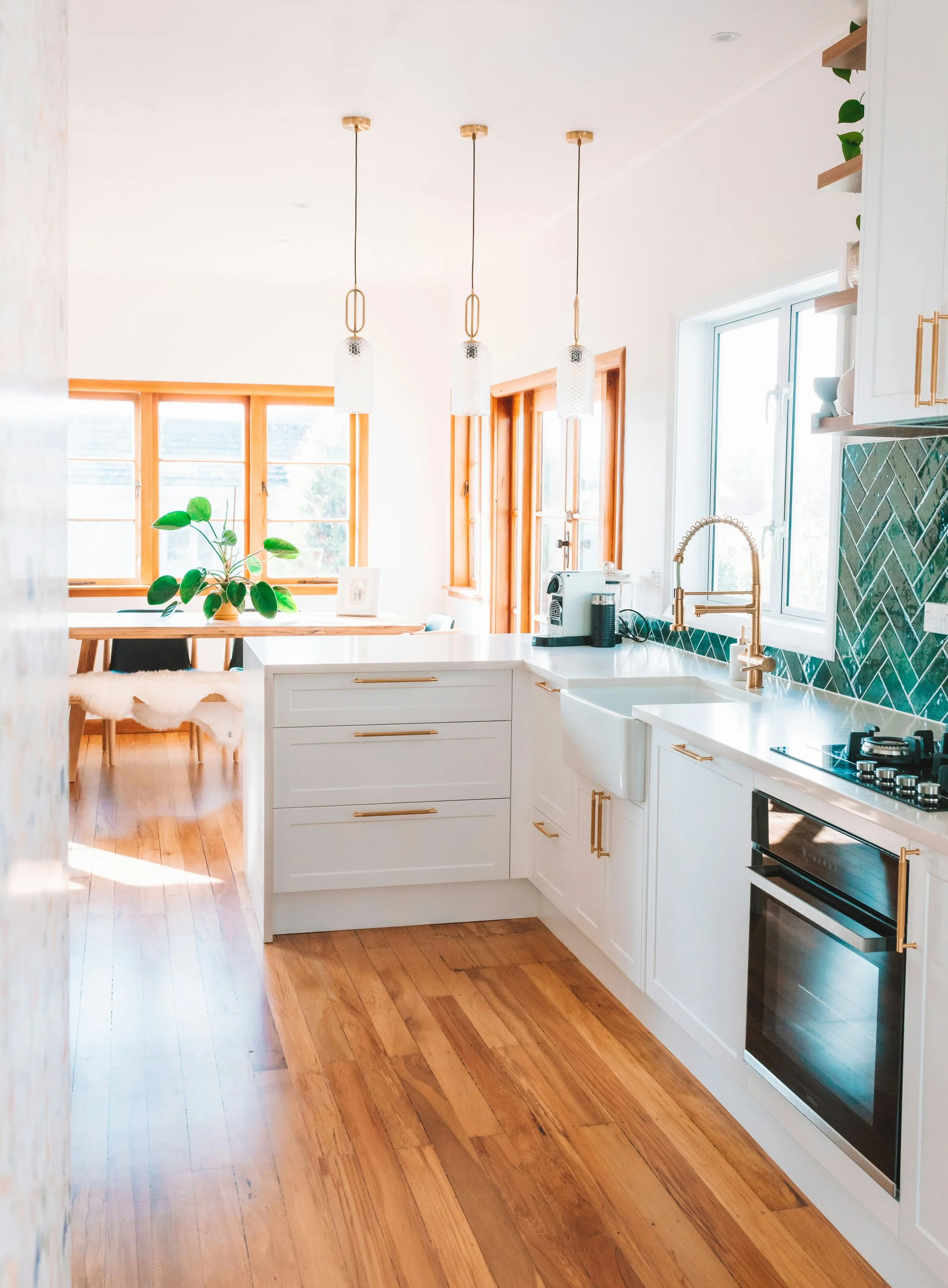 Bright kitchen with white cabinets, gold hardware, a window with wooden frames, a green plant, and three pendant lights hanging from the ceiling.
