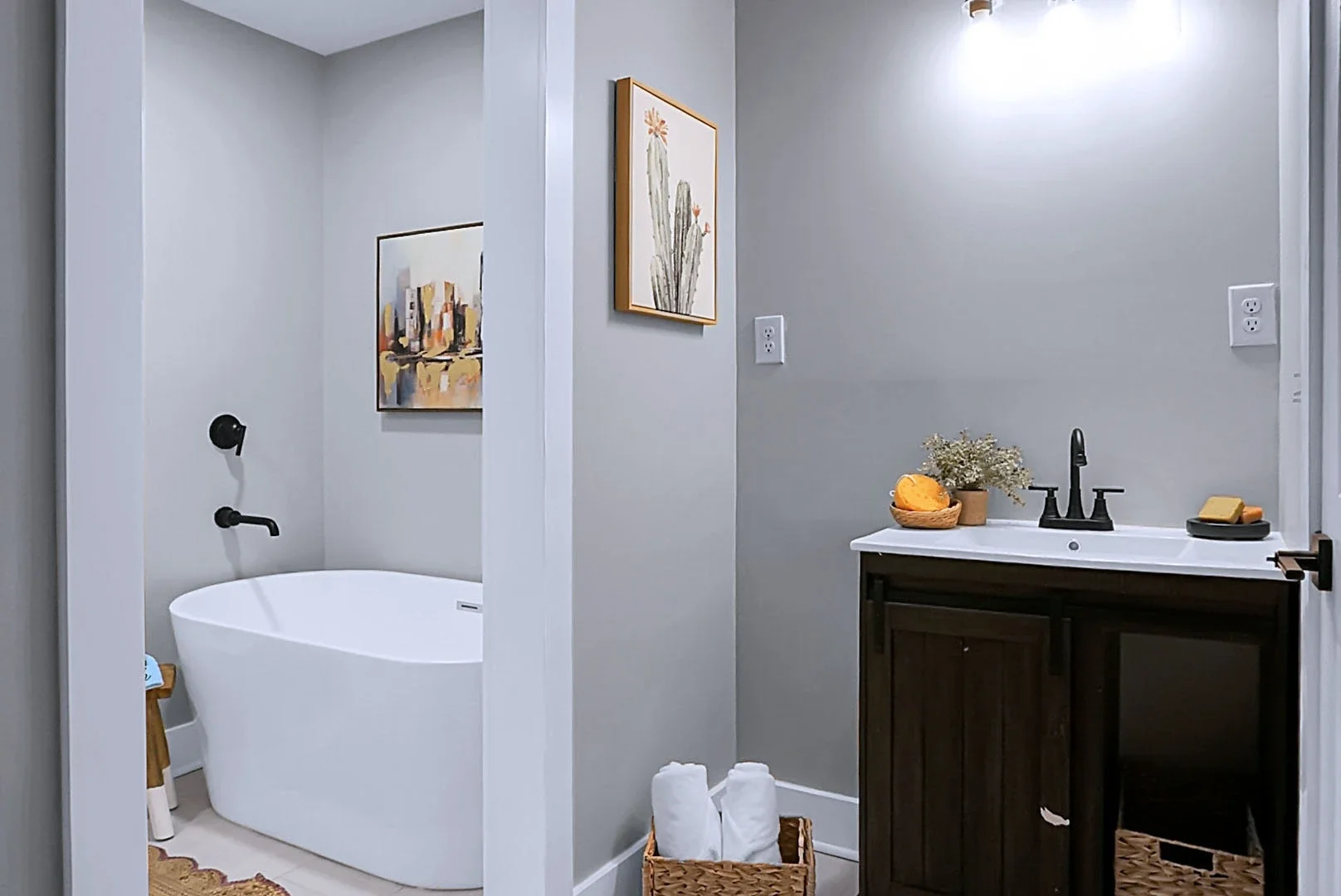 Bathroom with a bathtub, wall art, a vanity with a sink, black fixtures, decorative towels, and a basket of towels.