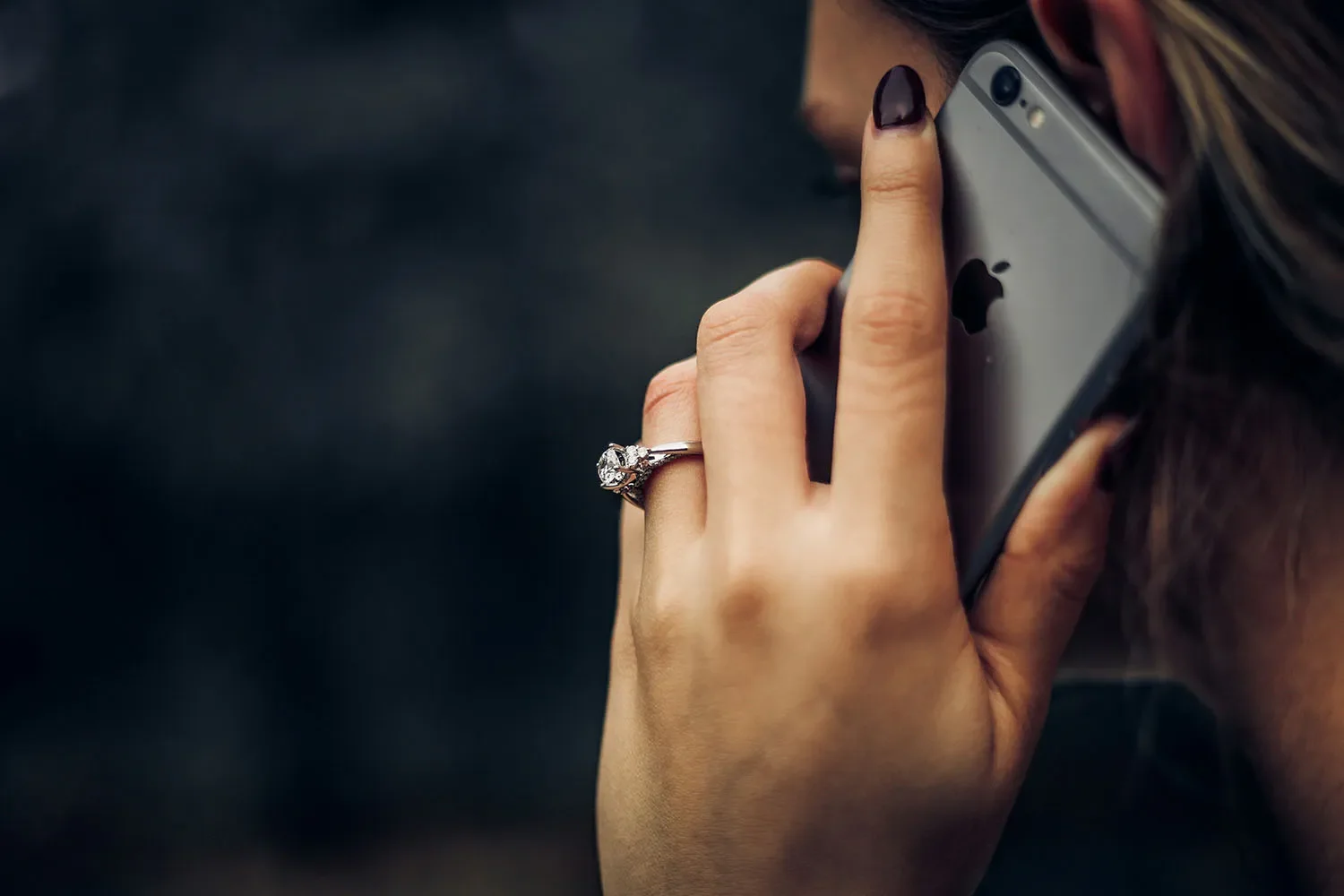 Close-up of a woman's hand holding an iPhone, showing a diamond engagement ring on her finger.