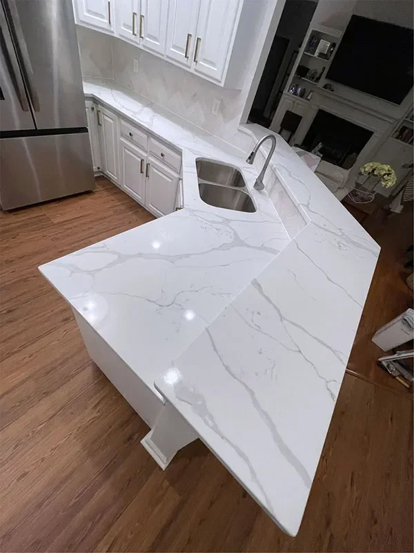A kitchen island with a white marble countertop and a built-in sink, situated in a modern kitchen with white cabinets and wooden flooring.