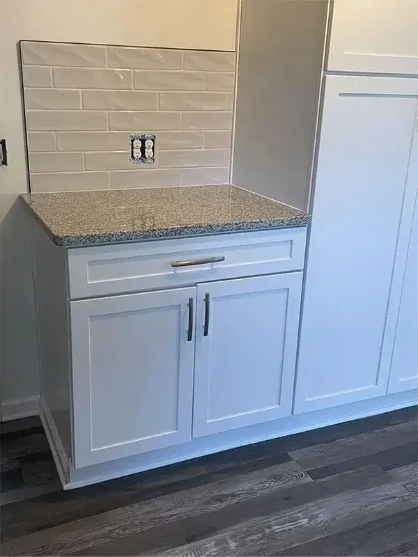 Kitchen cabinet with a granite countertop, beige subway tile backsplash, and a partially installed electrical outlet.
