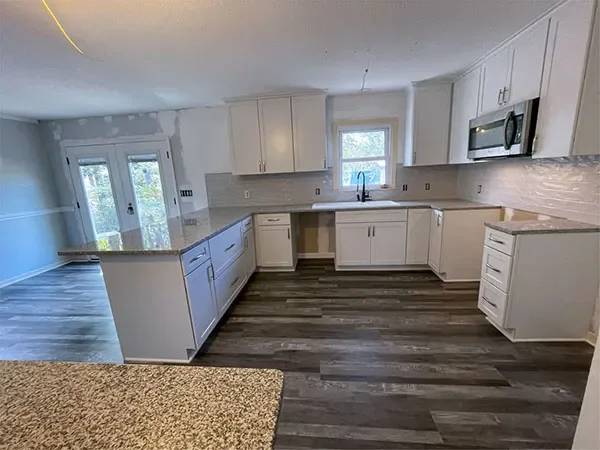 Modern kitchen with white cabinets, gray countertops, stainless steel microwave, and a window above the sink.