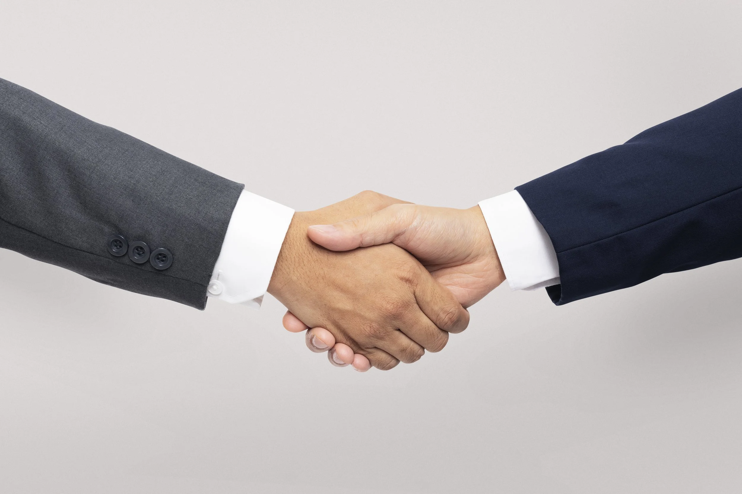 Deux personnes en costume se serrent la main, symbolisant un accord ou une entente.