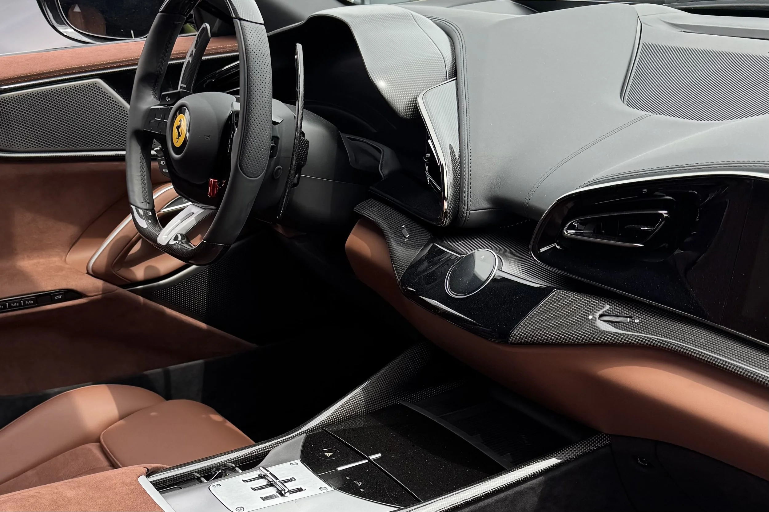 Intérieur d'une voiture de luxe, Ferrari, avec un tableau de bord en matériau composite, un volant à logo Ferrari, des sièges en cuir marron, et des finitions en carbone.