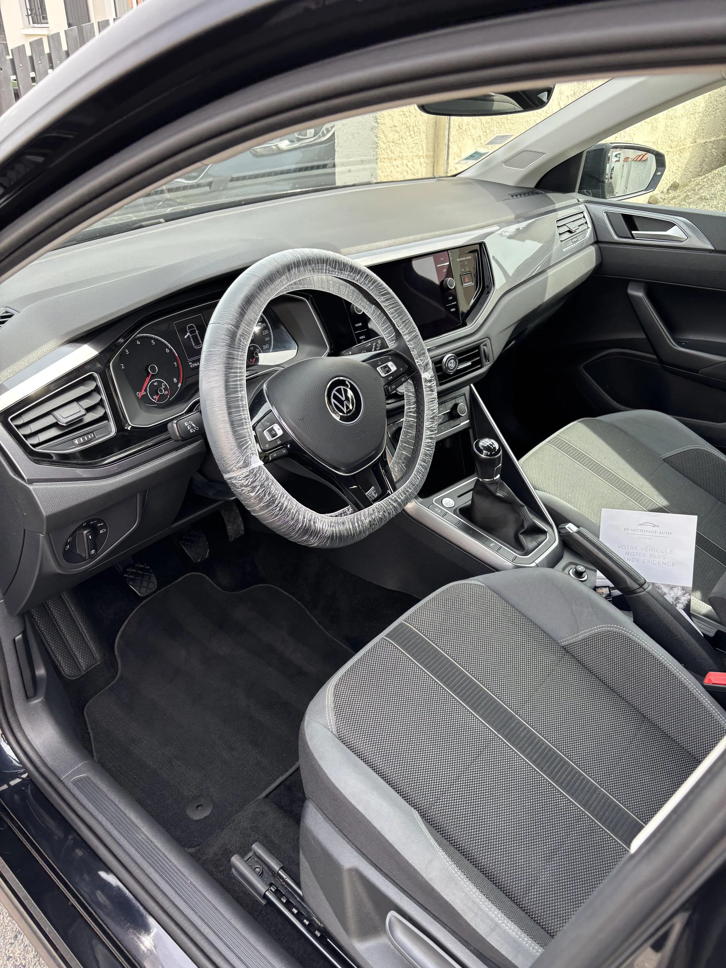 Intérieur d'une voiture Volkswagen avec le volant, le tableau de bord, l'écran central, le levier de vitesses, le siège conducteur et le siège passager. La voiture est propre et en stationnement.