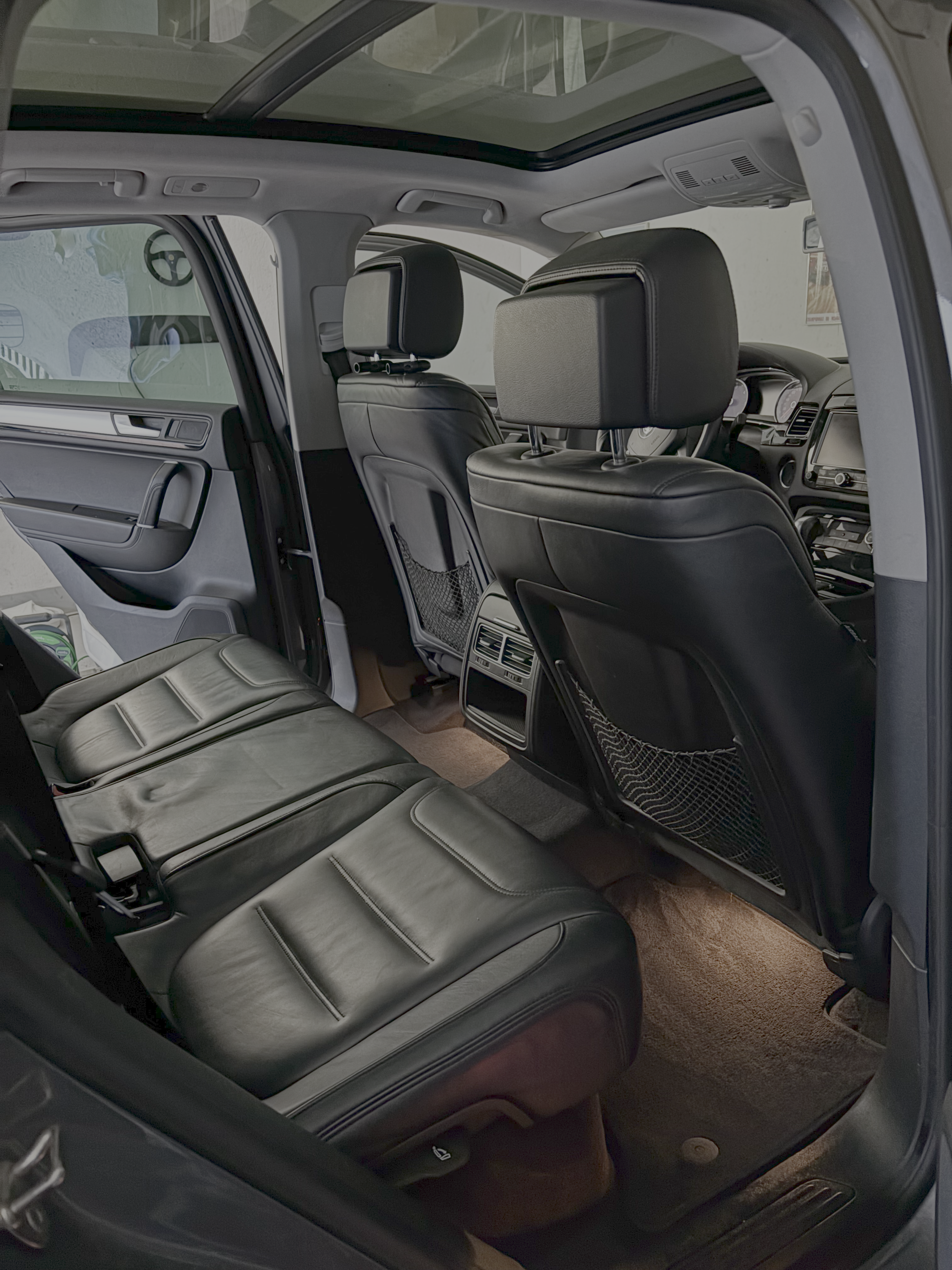 Intérieur d'une voiture avec sièges en cuir noir, vue de l'arrière, avec un plafond en verre, et des sièges d'avant équipés de têtes réglables.