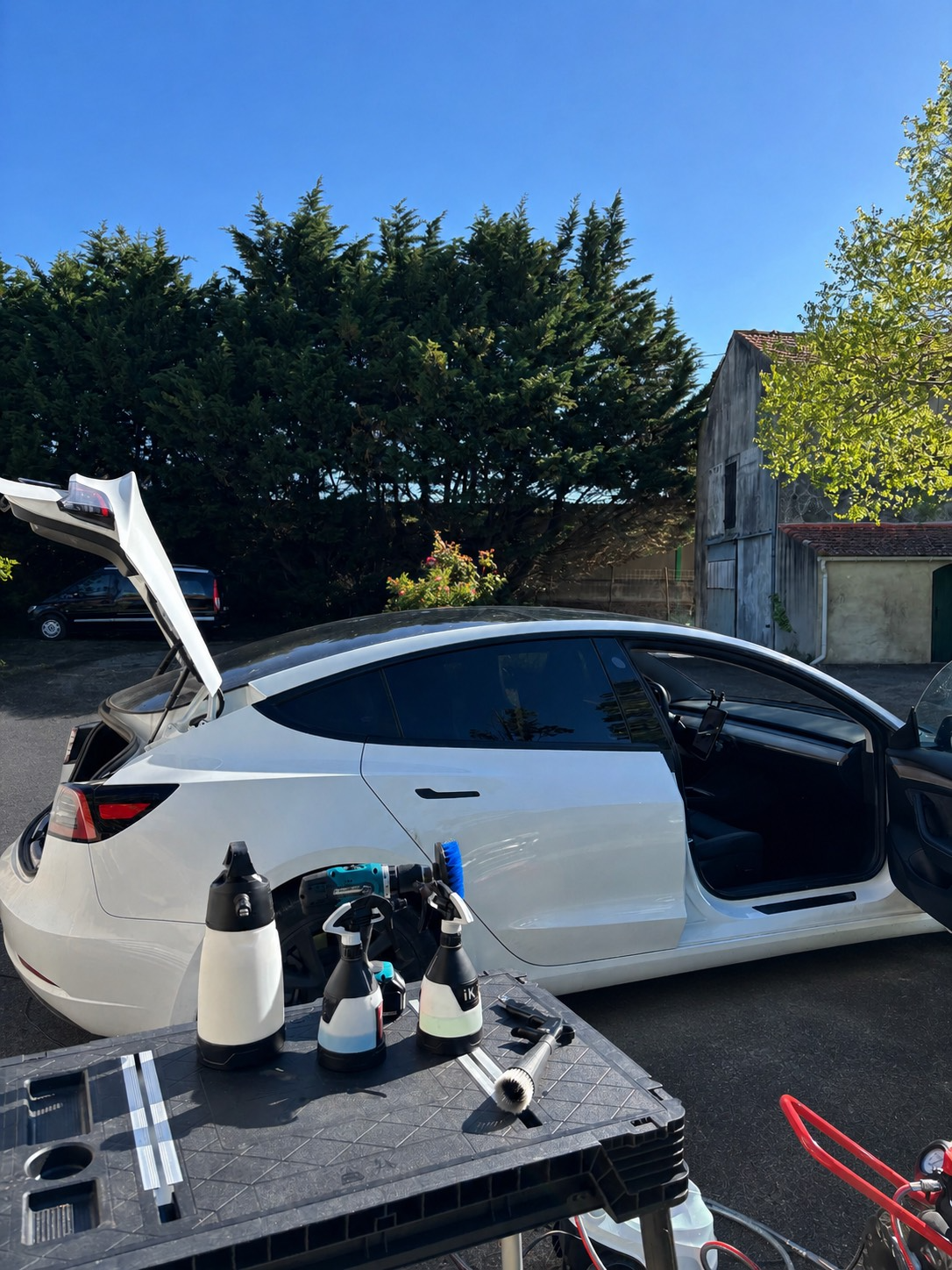 Voiture blanche en cours de nettoyage ou de detailing, avec des produits de nettoyage et des accessoires placés sur une table à proximité.