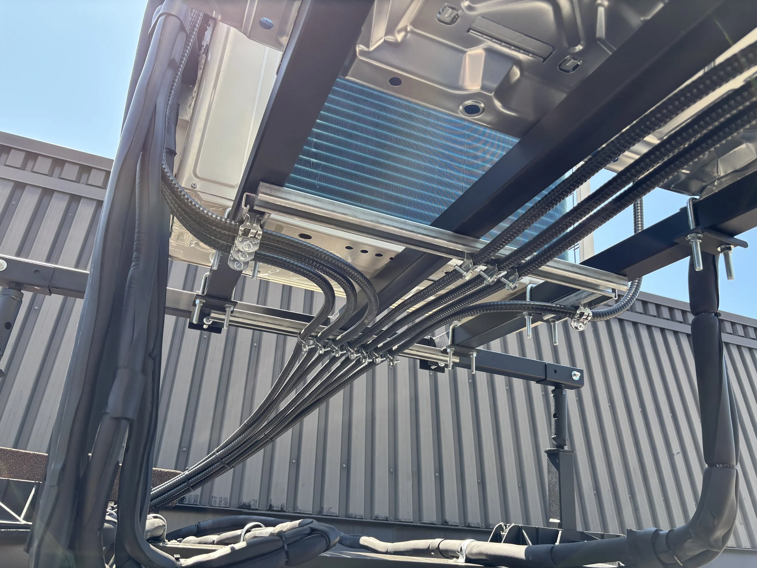 Close-up of industrial equipment with metal pipes, wiring, and a radiator or heat exchanger against a blue sky background.