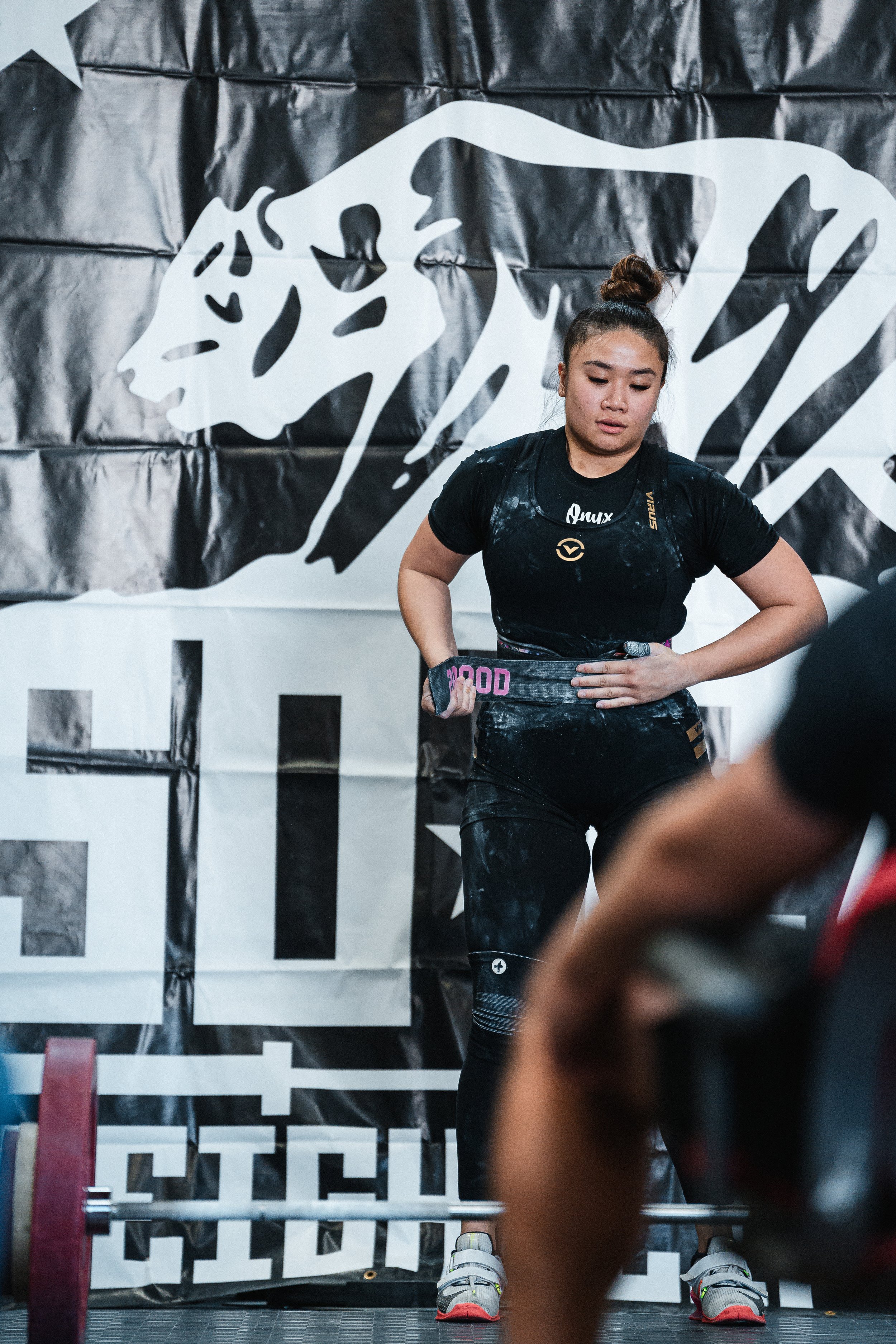 Female weightlifter after a lift at a competition, standing in front of a lion logo banner.
