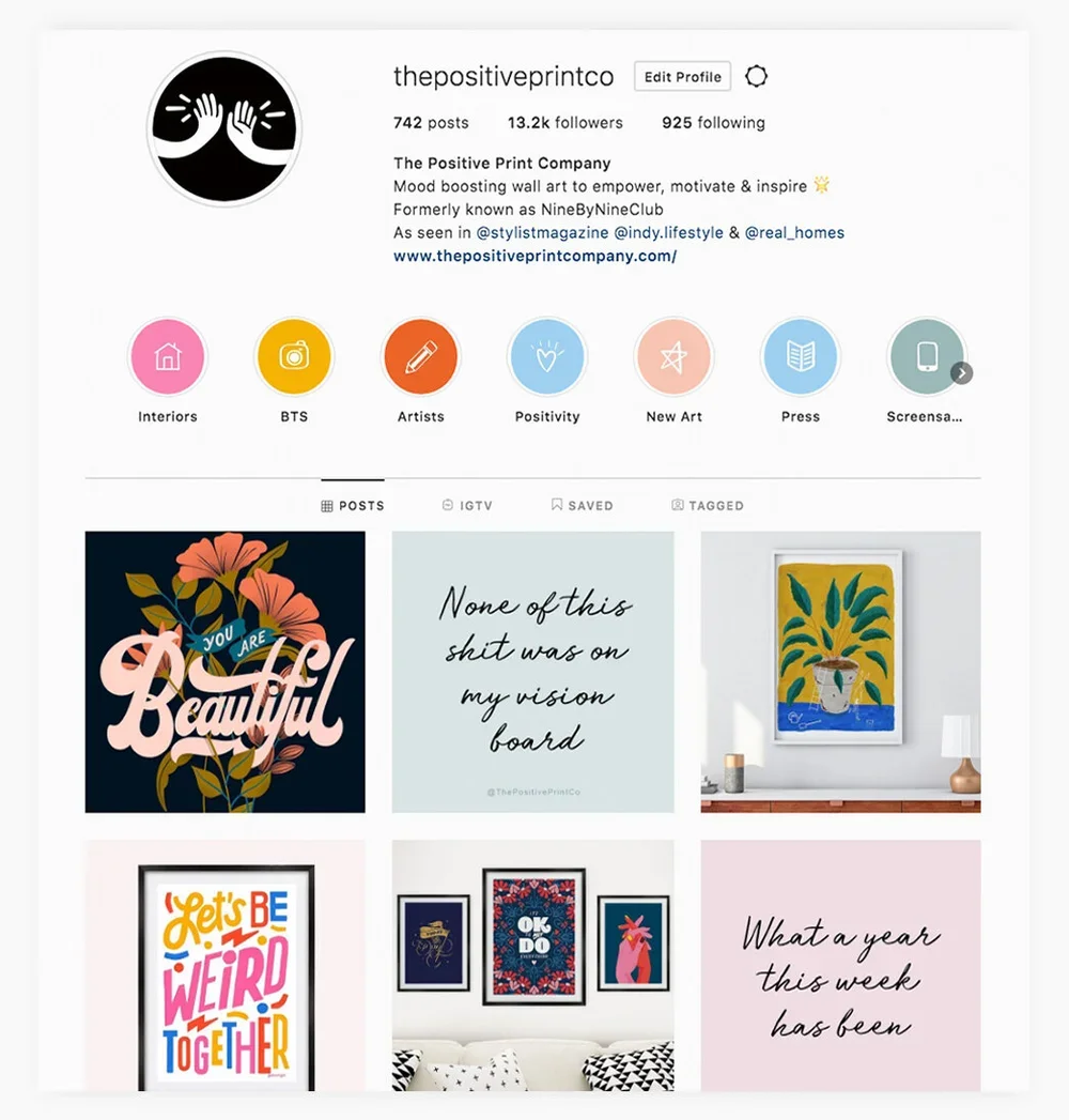 Instagram profile page of thepositiveprintco, a company that creates mood-boosting wall art. The profile features a black and white logo of two hands high-fiving. There are six circular highlight icons for Interiors, BTS, Artists, Positivity, New Art, Press, and Screenplays. The posts display colorful artwork and inspirational quotes, including one that says 'You Are Beautiful' and another that reads 'None of this shit was on my vision board.'