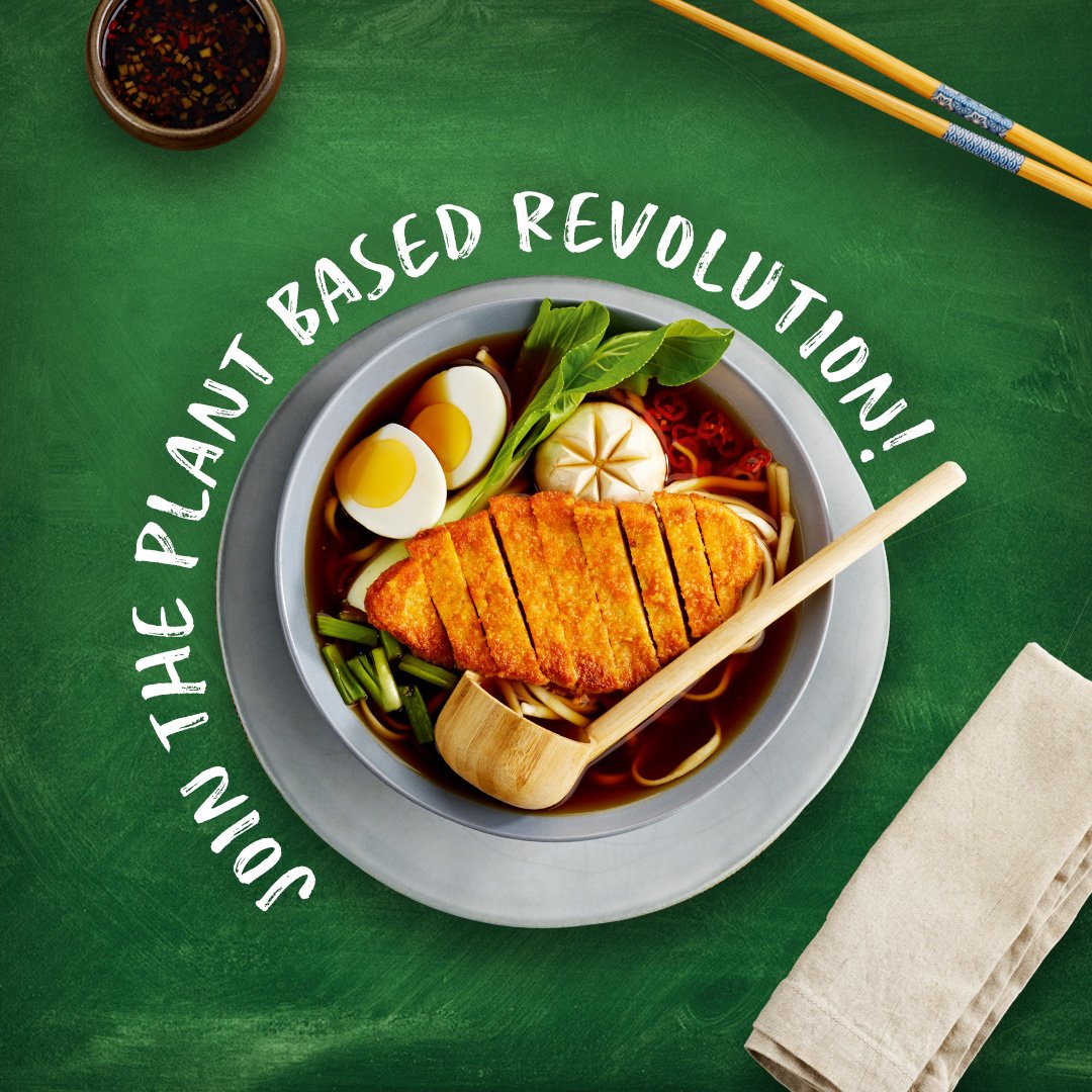 A bowl of ramen with sliced boiled eggs, green leafy vegetables, a piece of fried chicken, garlic, and red peppers on a green table, with chopsticks, a wooden spoon, a small bowl of dipping sauce, and a beige napkin nearby. Text over the image reads, "Join the planet based revolution!"