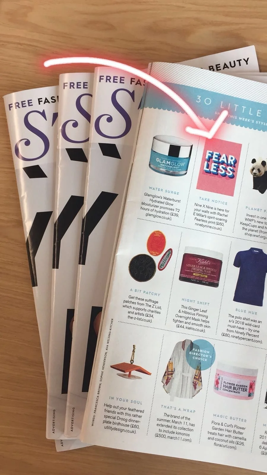 Stack of magazines spread on a wooden surface, featuring beauty and lifestyle content, with some pages displaying product ads and thematic sections.