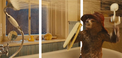 A bear in a bathroom holding a toothbrush and wearing a red bandana or hat.