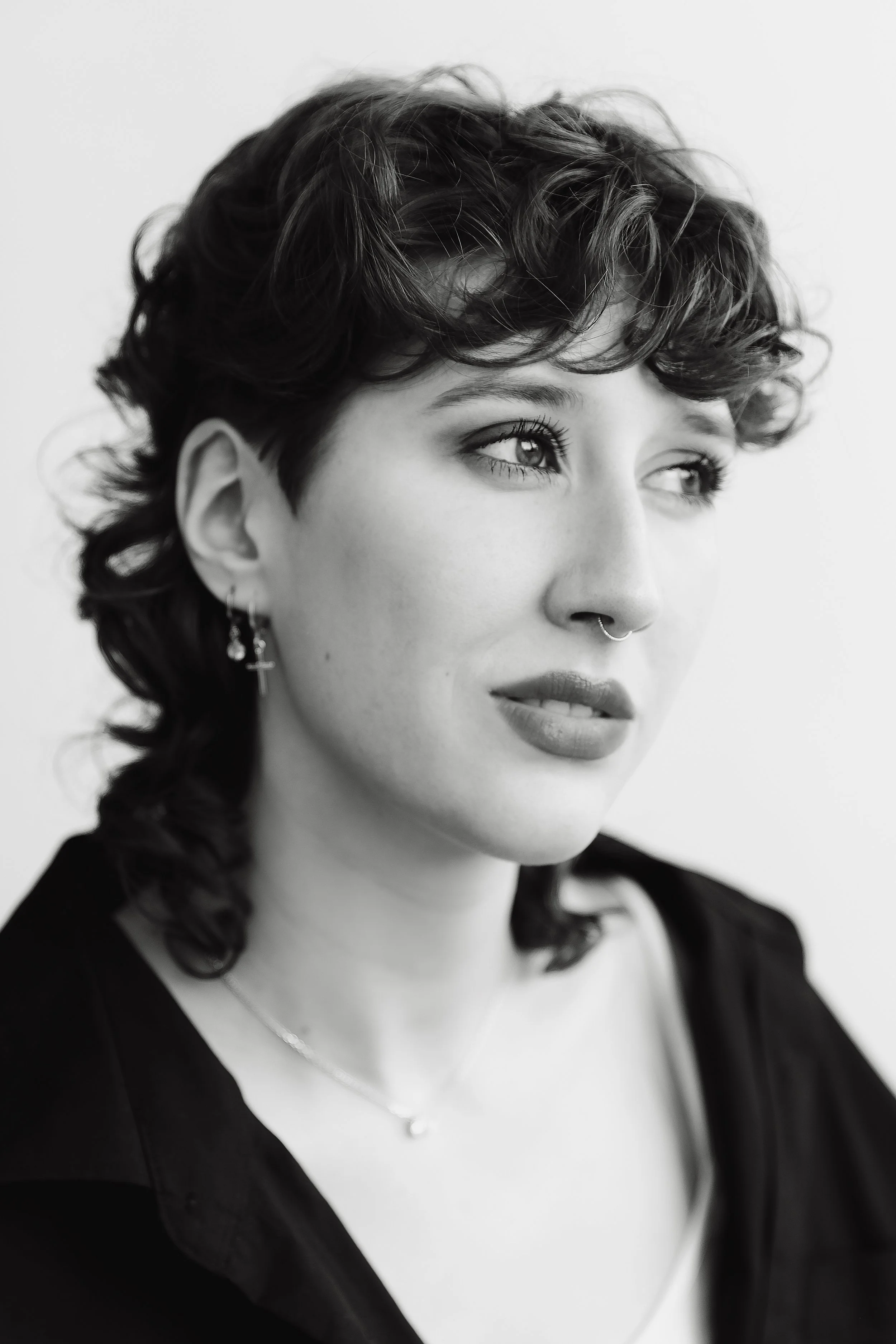 Schwarzkopf Portrait einer jungen Frau mit kurzen, lockigen Haaren, Piercings, und Earring, in Schwarz-Weiß-Fotografie.