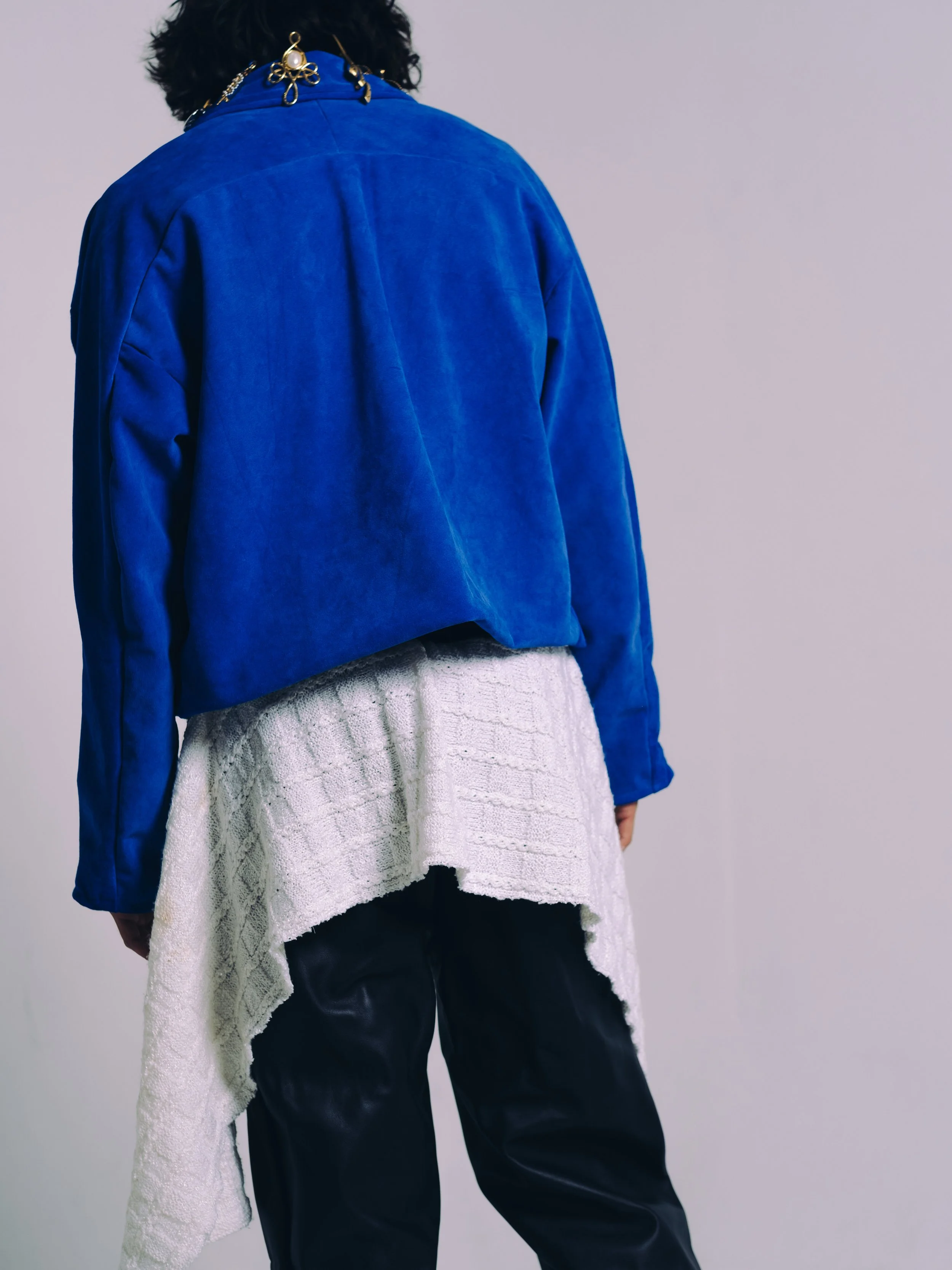 Person wearing a blue jacket, white textured sweater, and black pants, with a decorative gold earring and chain.