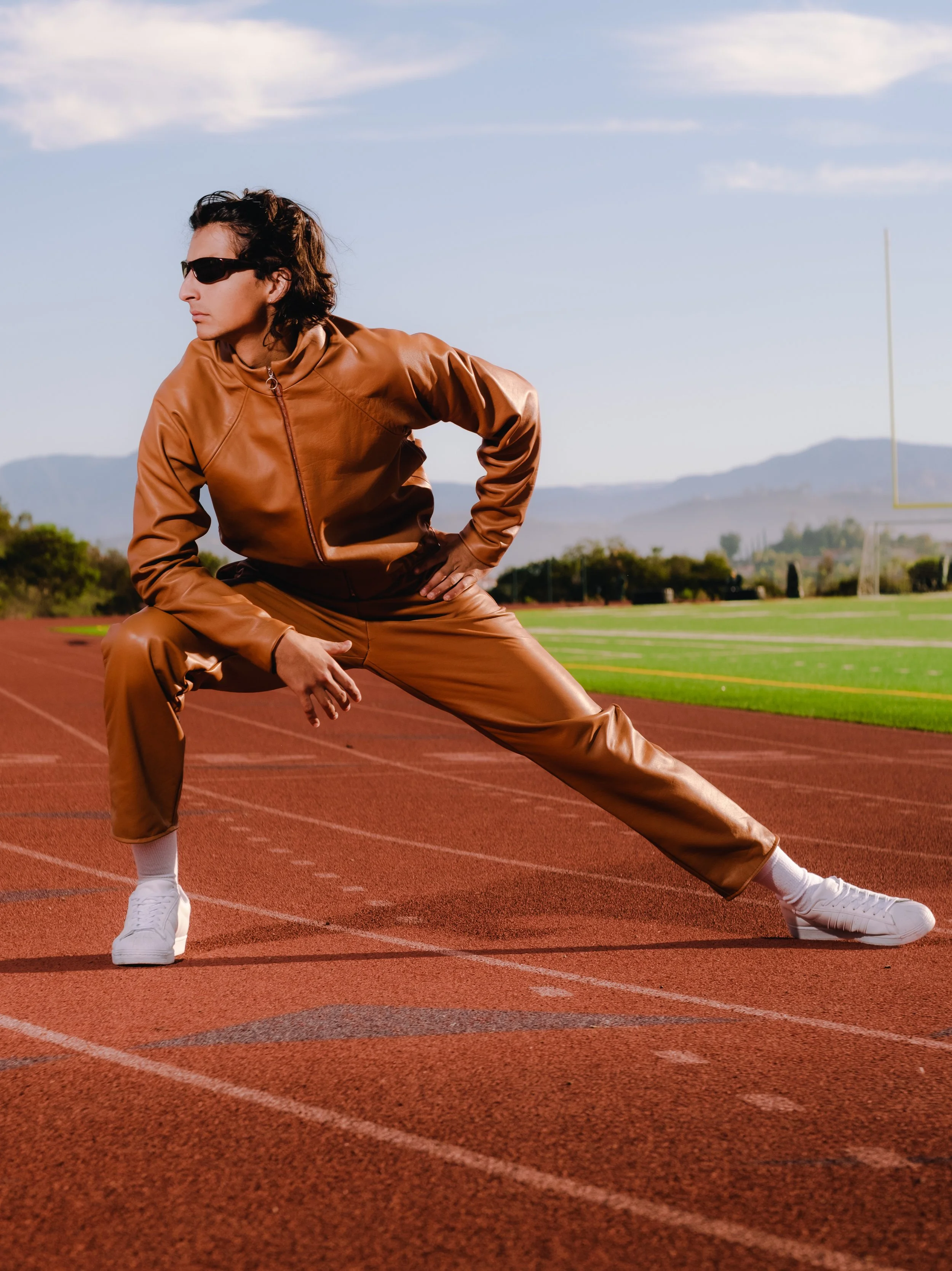 A person in athletic clothing and sunglasses stretches on a running track outdoors.