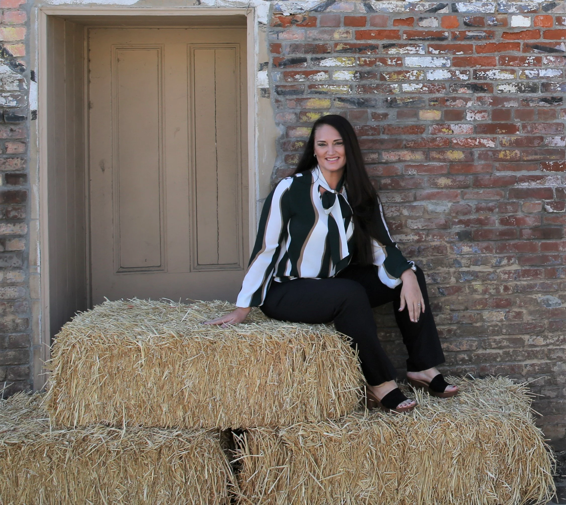 A woman sitting on a stack of hay bales in front of a brick wall.