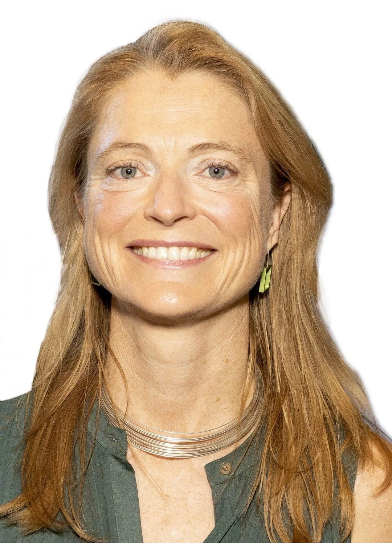 A woman with long red hair, blue eyes, and a big smile, wearing a dark green shirt, gold earrings, and a metallic necklace