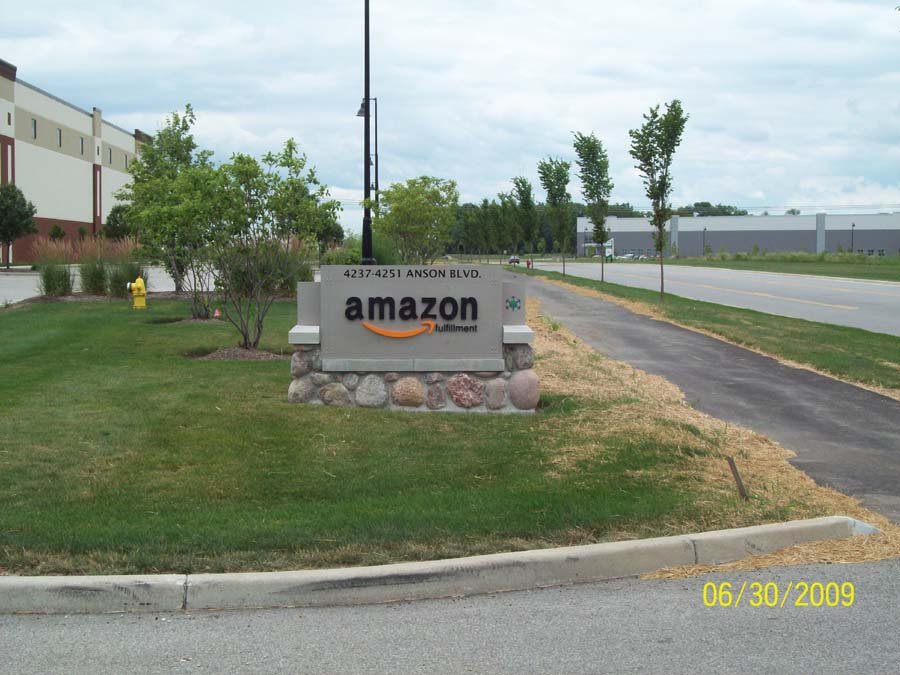 Sign for Amazon Fulfillment located at 4237-4251 Anson Blvd. in a landscaped area with grass, trees, and shrubs, next to a paved sidewalk and road, with industrial buildings in the background, under a cloudy sky. Date stamp: June 30, 2009.