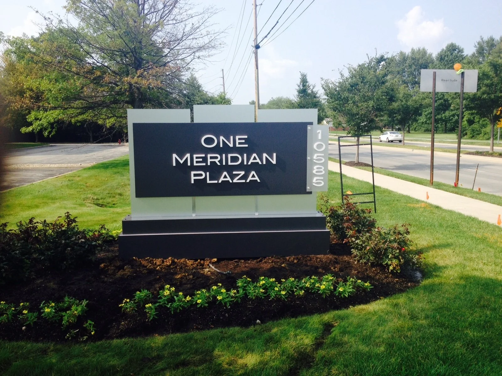 Sign for One Meridian Plaza with address 10506 on a grassy area with trees and street in background.