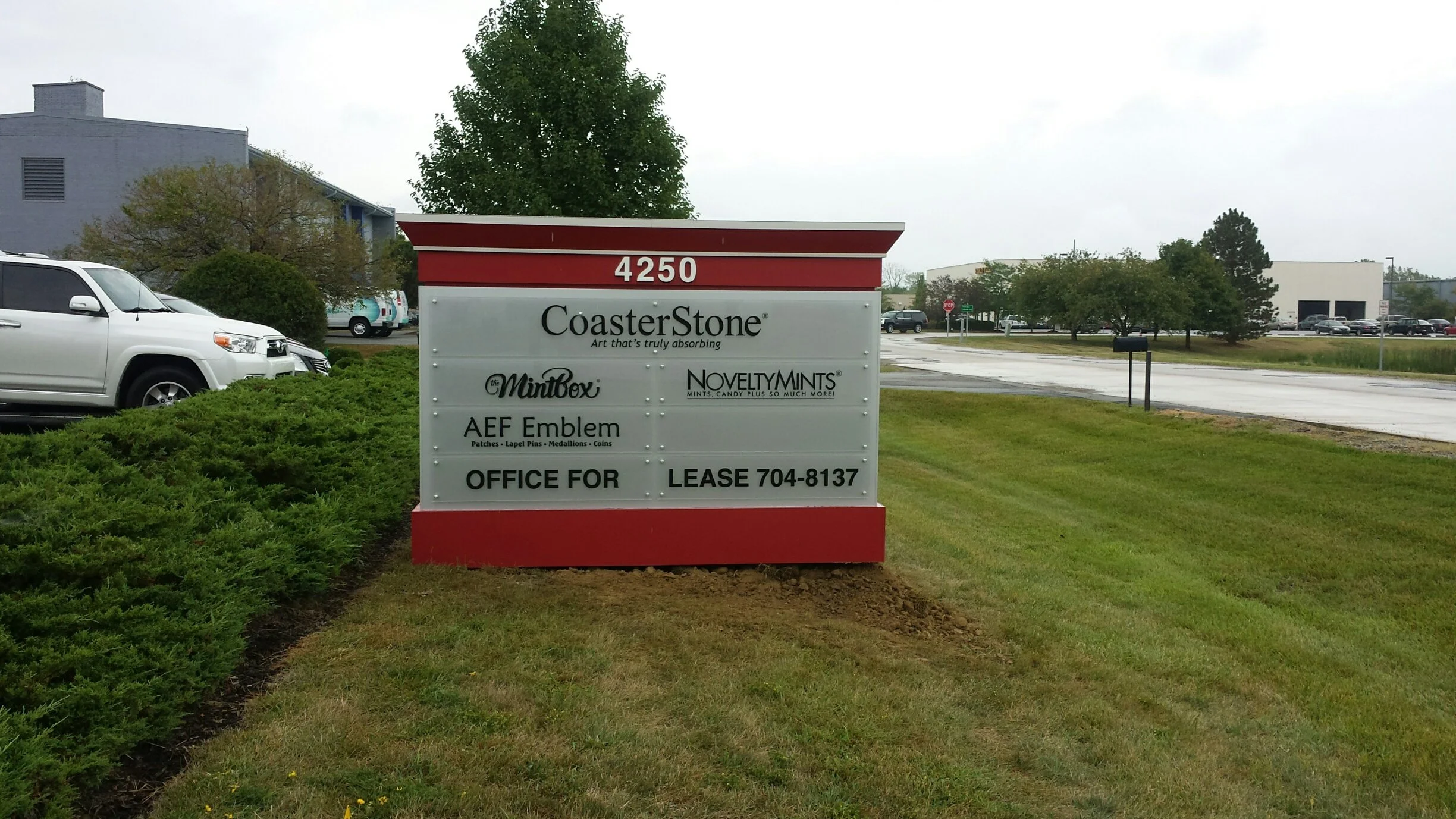 Sign for CoasterStone company with listing for office space lease, located at 4250, surrounded by green lawn and parking lot in background.