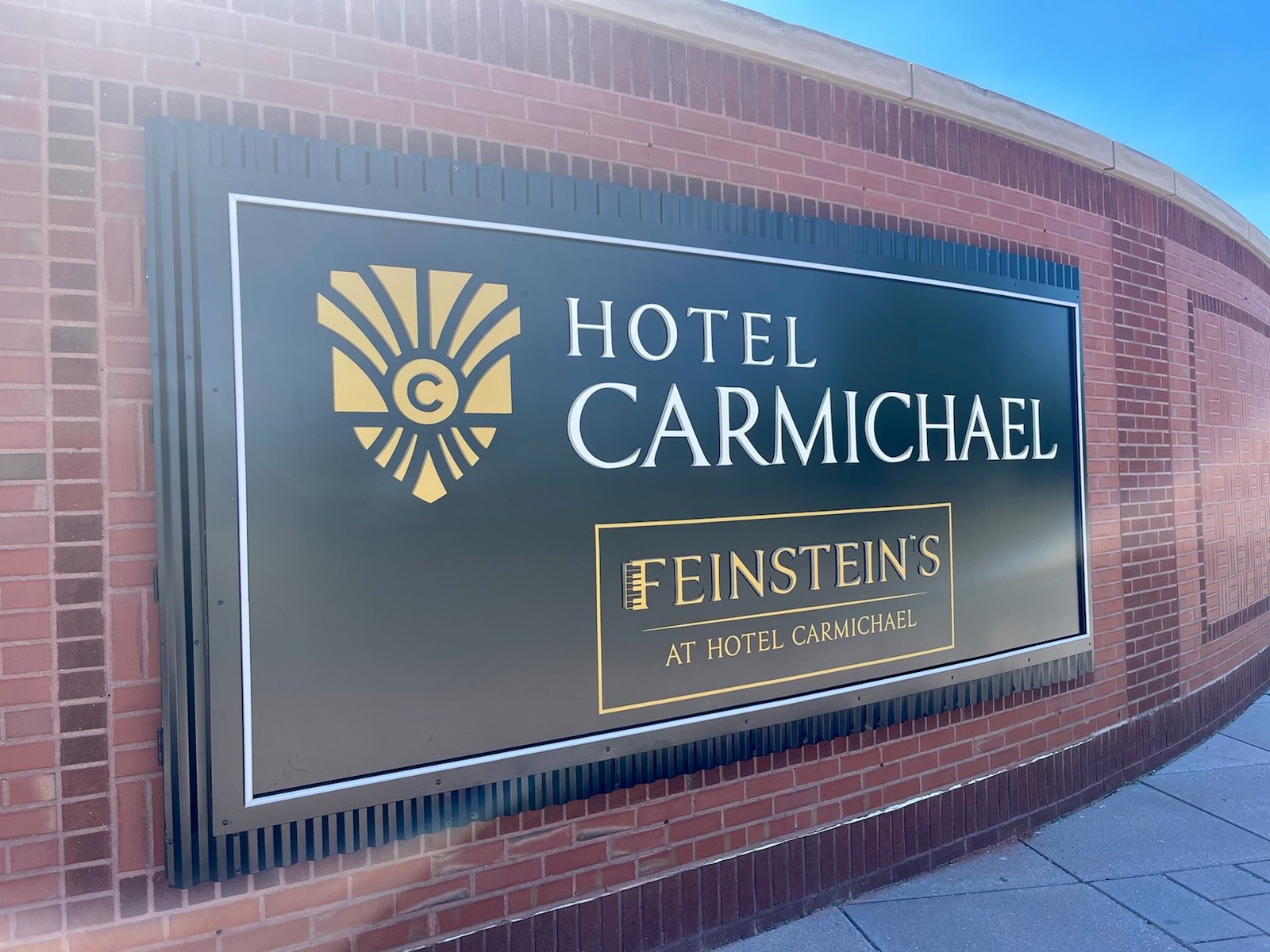 A sign on a brick wall reading 'Hotel Carmichael at Feinstein's' with a gold and black logo.