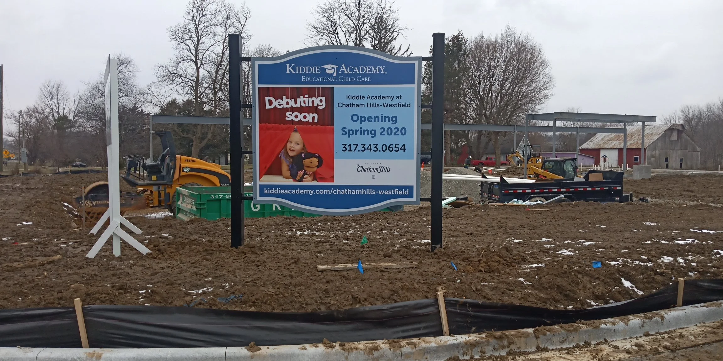 Construction site with a sign announcing the upcoming opening of Kiddie Academy at Chatham Hills-Westfield in spring 2020, surrounded by earth-moving equipment and partially built structures.