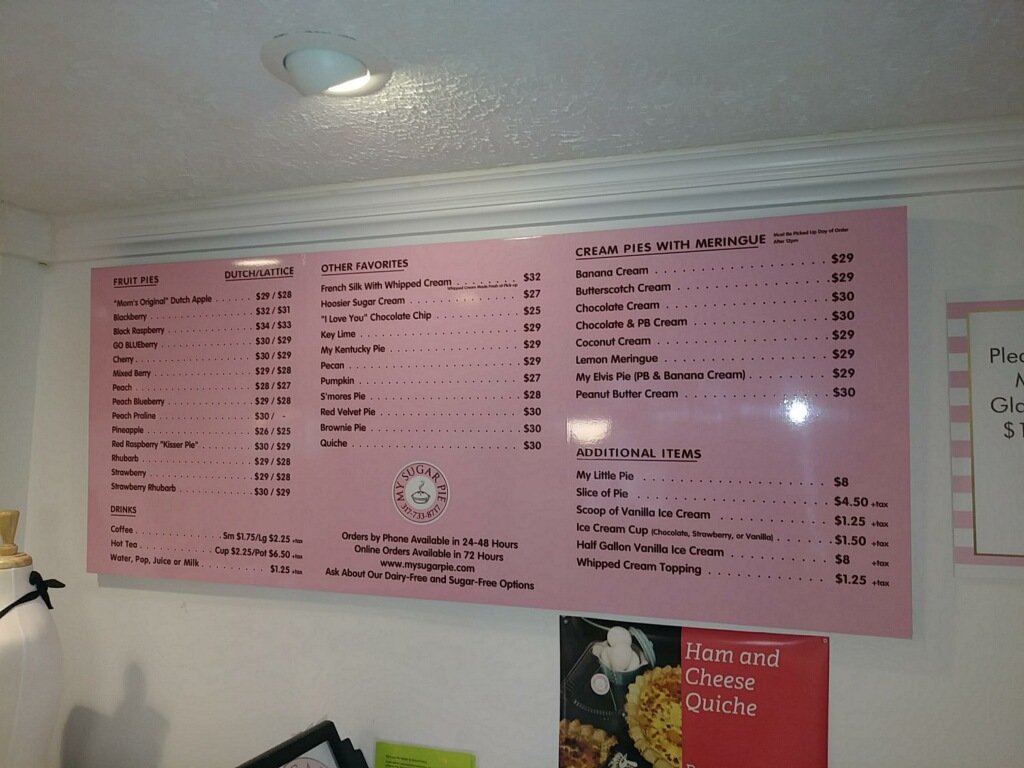 Pink menu board featuring various fruit pies, cream pies with meringue, and other desserts with prices listed.