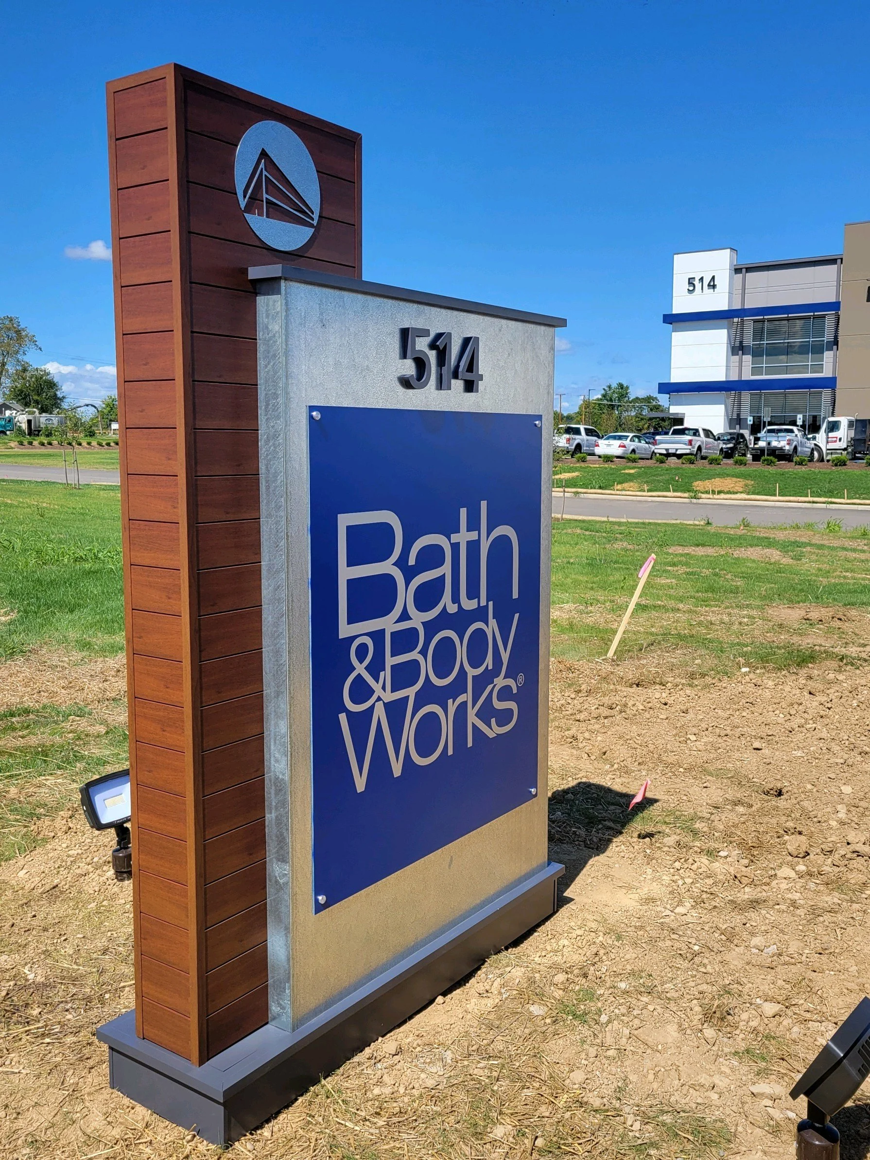 A standing sign with the logo and name of Bath & Body Works, displaying the street number 514, outdoors on a sunny day.