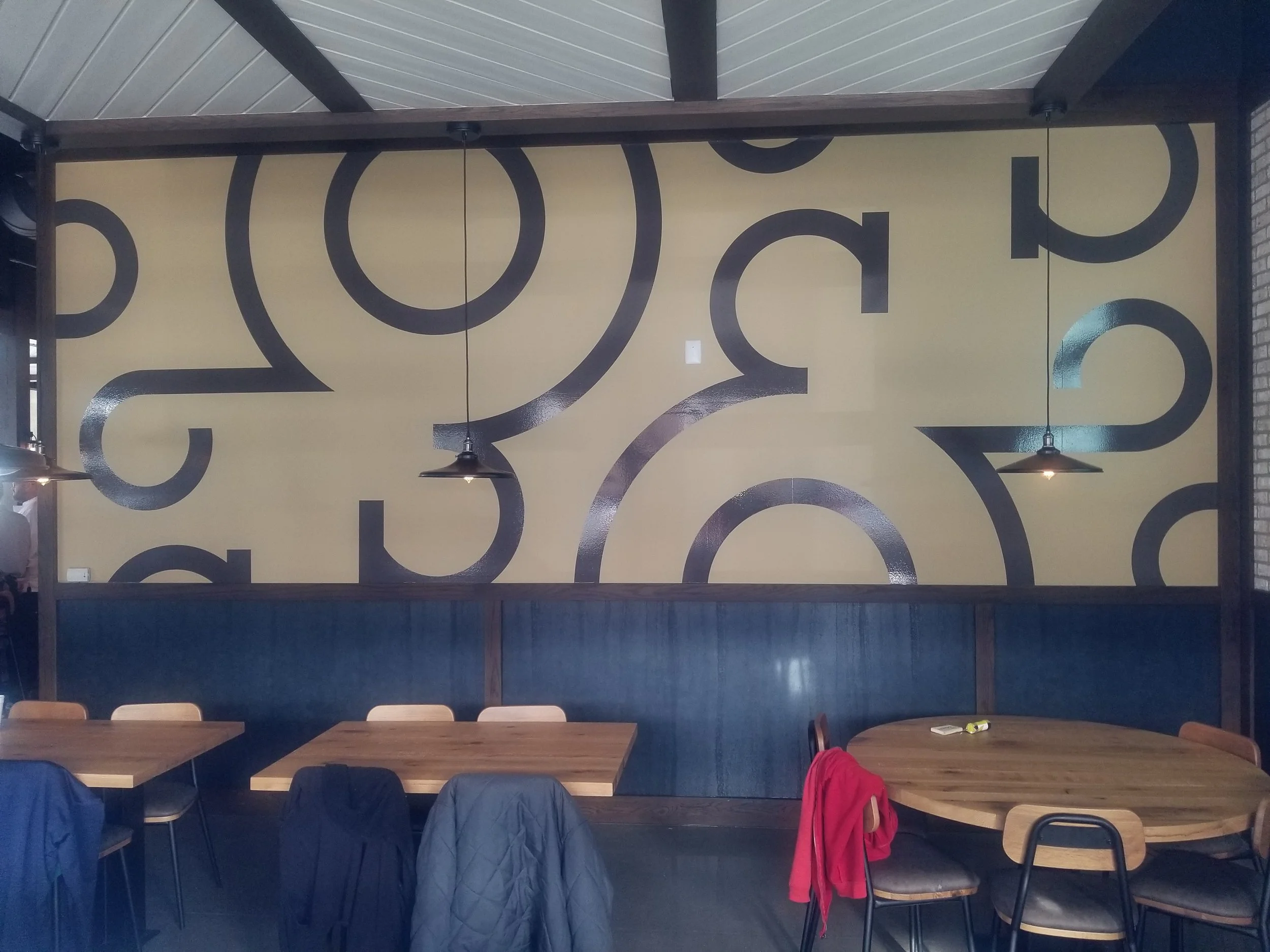 Interior of a restaurant with a large abstract mural on the wall, wooden tables, and chairs with jackets hanging on some of them.