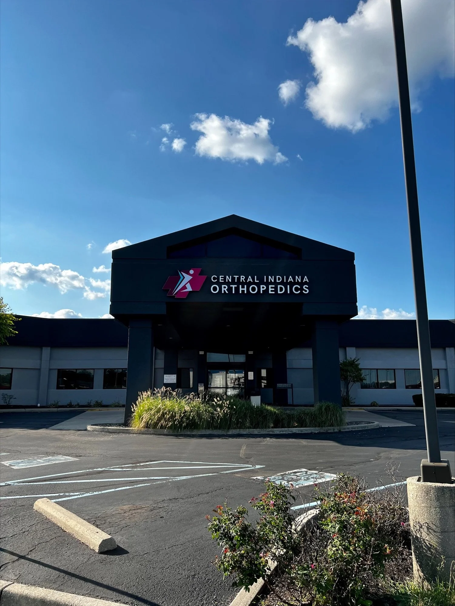 Exterior view of Central Indiana Orthopedics building with a parking lot in front and blue sky with clouds overhead.