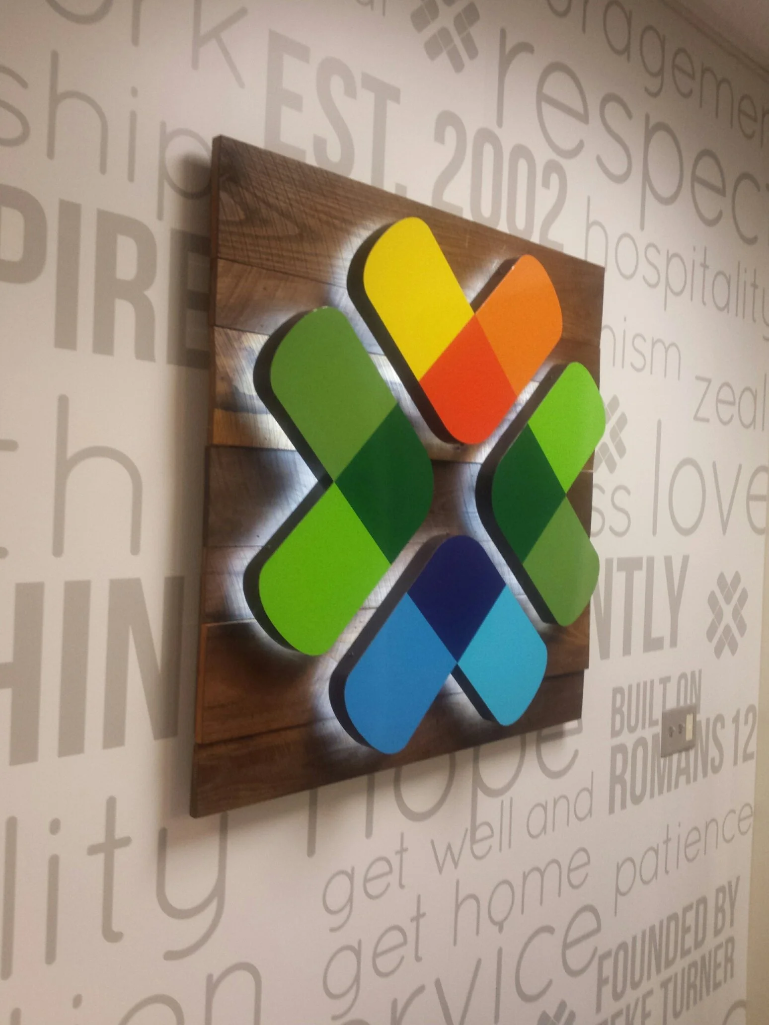 Colorful geometric logo on a wooden panel with a wall background featuring words and phrases.