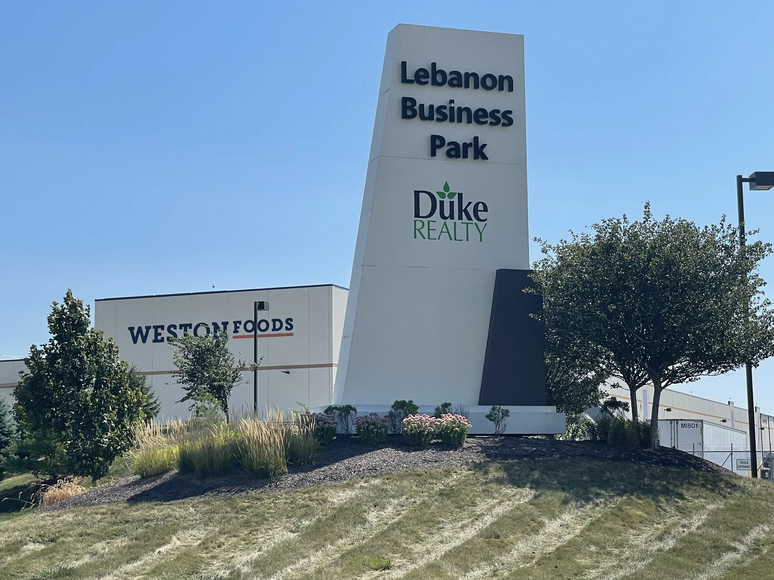 Entrance sign for Lebanon Business Park with Duke Realty logo, located near Weston Foods building, trees, grass, and landscaping.