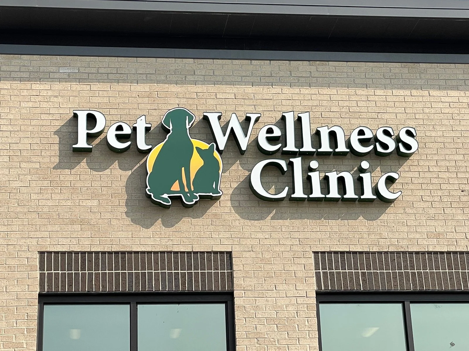 Sign for Pet Wellness Clinic with silhouettes of a dog and a cat in front of a yellow circle on a brick wall.