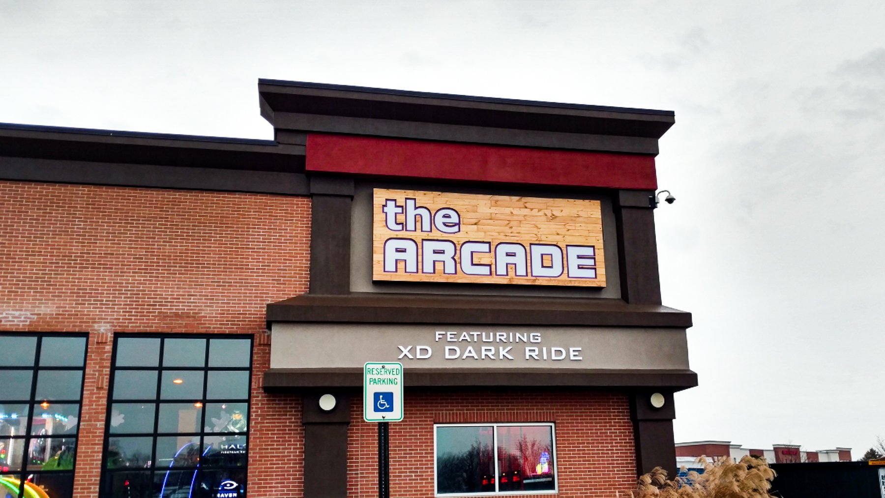 Exterior view of a building with a sign that reads 'the ARCADE' and a subtitle mentioning 'featuring XD DARK RIDE', with a reserved handicap parking sign in front.