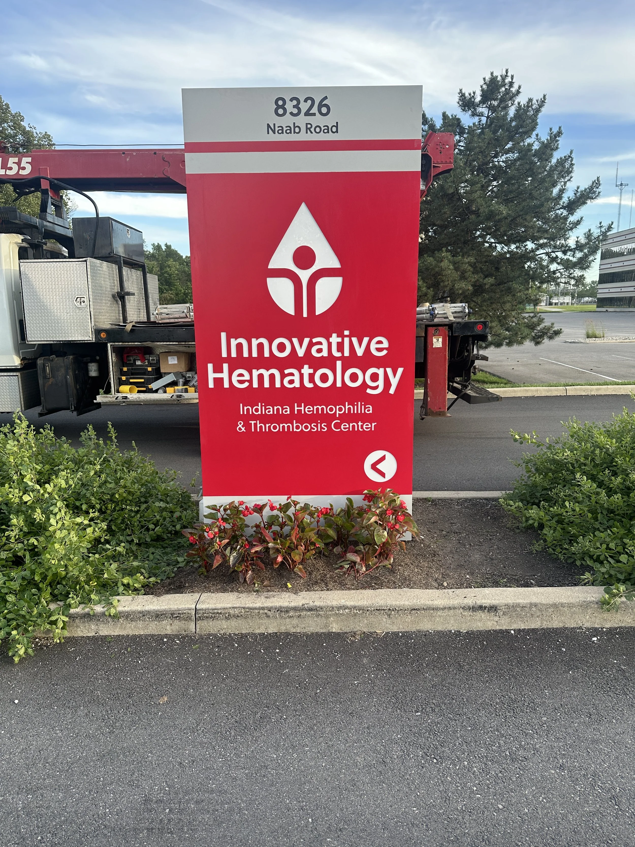 Sign for Innovative Hematology and Indiana Hemophilia & Thrombosis Center at 8326 Naab Road, with some bushes and a parking lot.