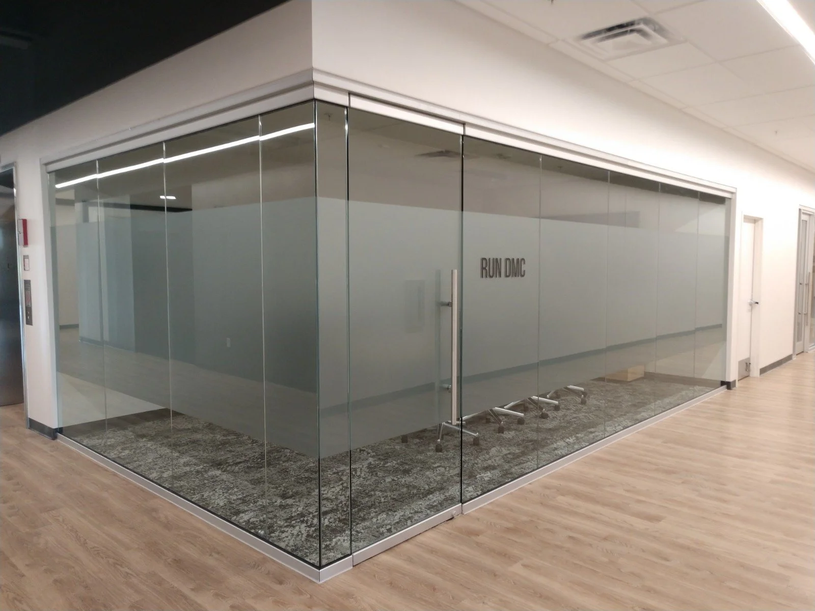 Empty office meeting room with glass walls, four office chairs, a small rug, and a sign that says "RUN DMC" on the wall.